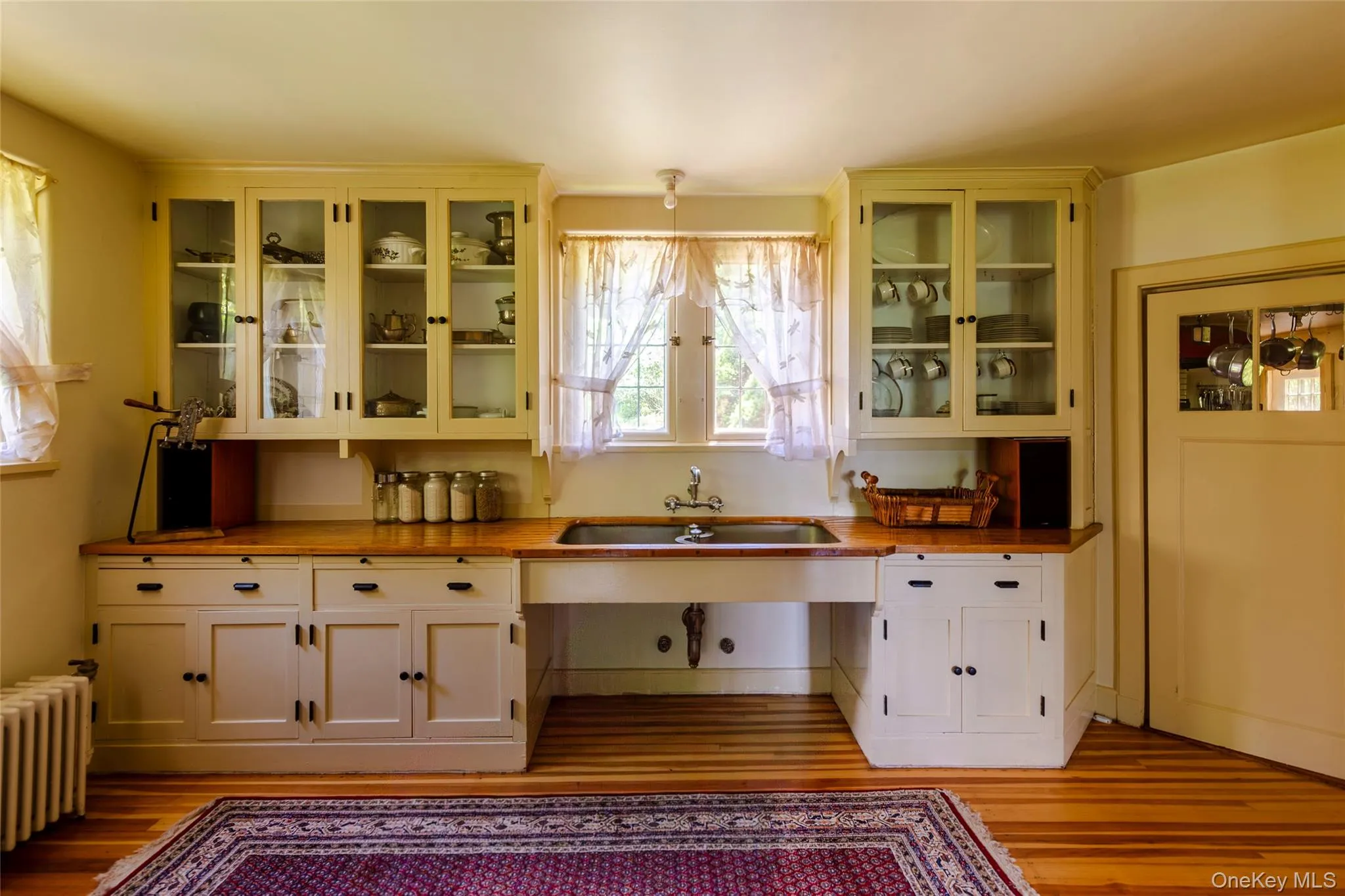 Kitchen featuring wood counters, radiator heating unit, glass insert cabinets, and light wood-type flooring Kitchen featuring wood counters, radiator heating unit, glass insert cabinets, and light wood-type flooring