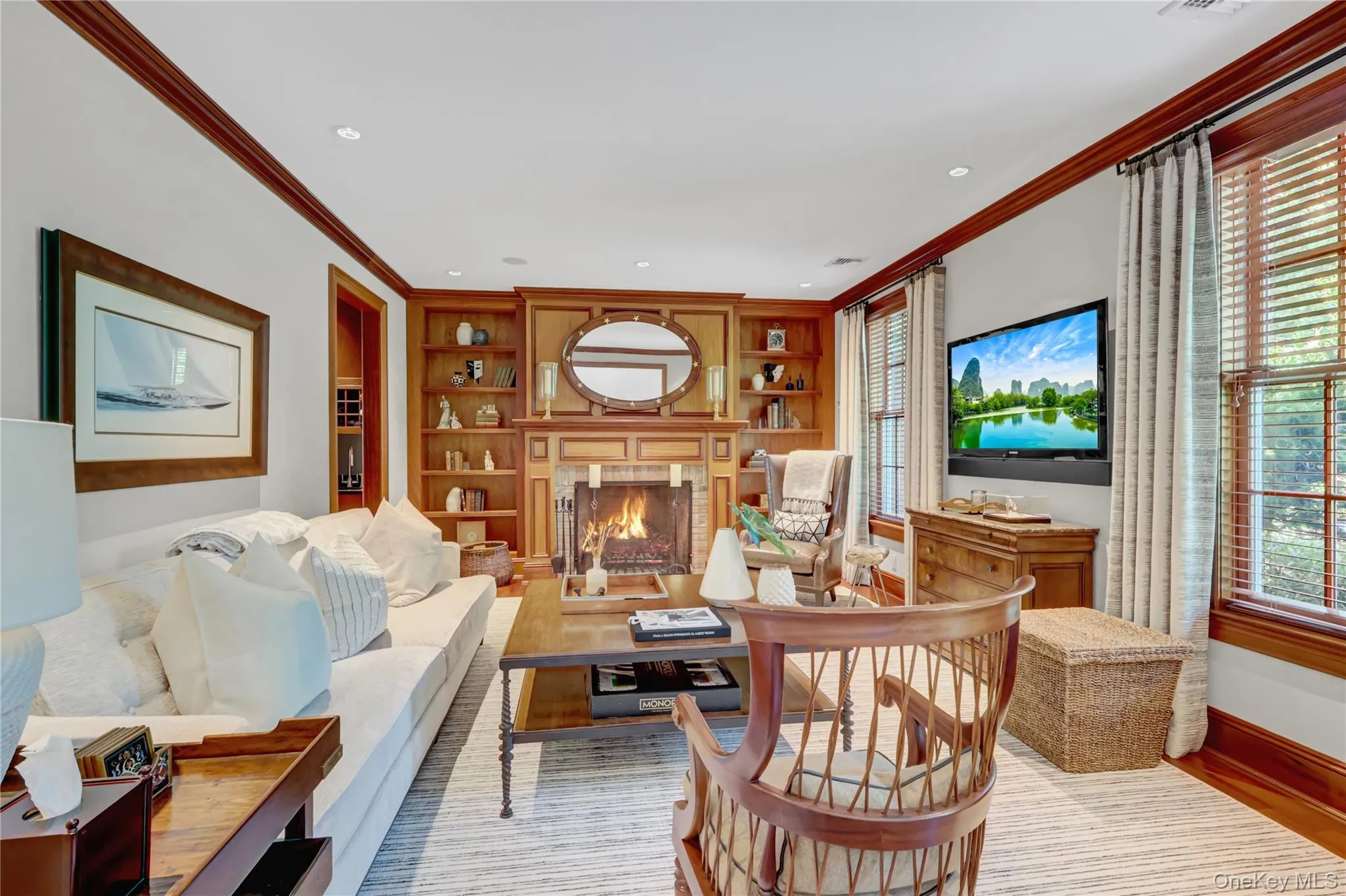 Living room featuring built in shelves, crown molding, light wood finished floors, plenty of natural light, and a lit fireplace Living room featuring built in shelves, crown molding, light wood finished floors, plenty of natural light, and a lit fireplace