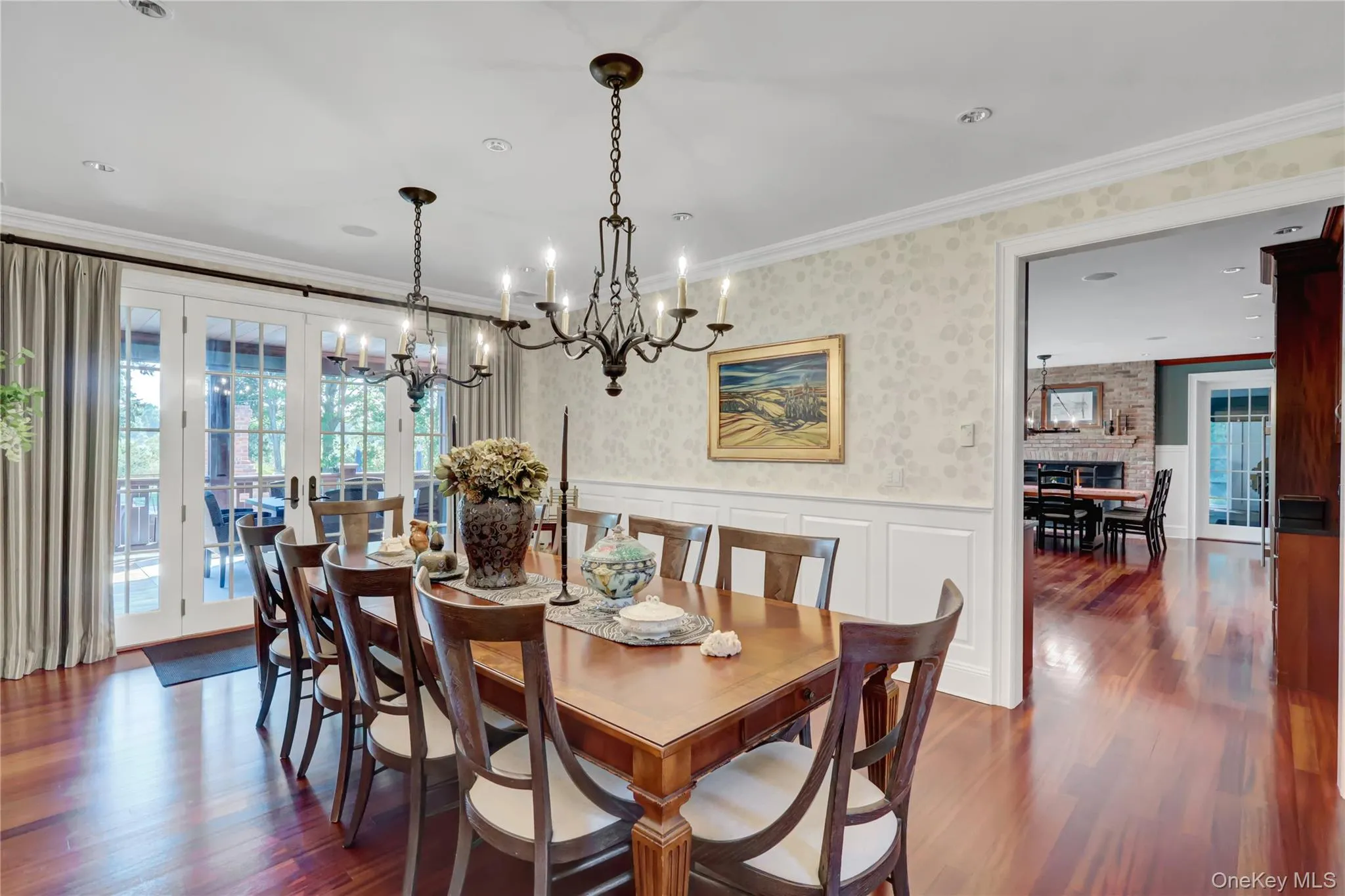 Dining room featuring wallpapered walls, a wainscoted wall, dark wood finished floors, crown molding, and a decorative wall Dining room featuring wallpapered walls, a wainscoted wall, dark wood finished floors, crown molding, and a decorative wall