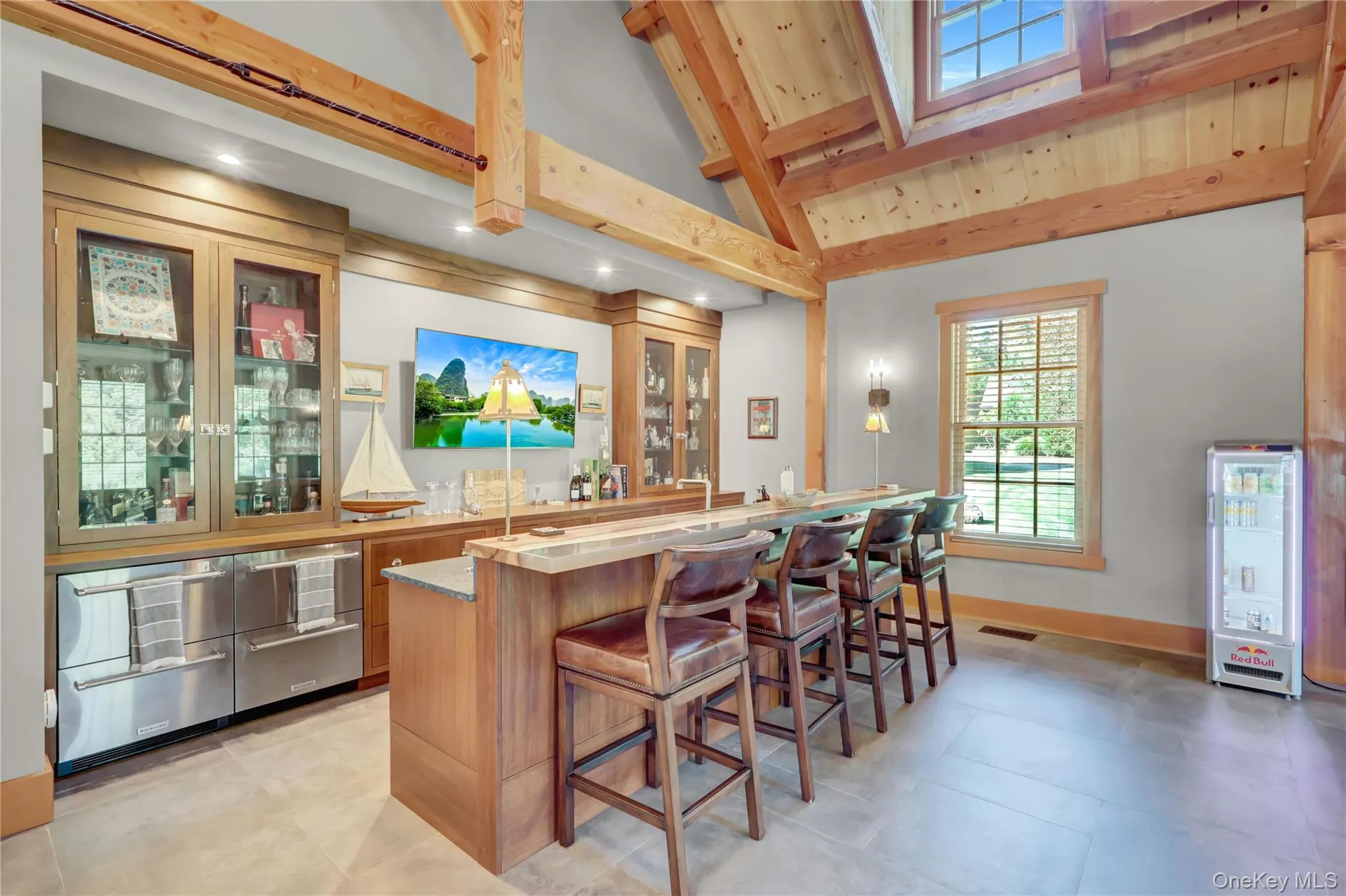 Indoor wet bar featuring glass insert cabinets, brown cabinets, beamed ceiling, high vaulted ceiling, and light stone counters Indoor wet bar featuring glass insert cabinets, brown cabinets, beamed ceiling, high vaulted ceiling, and light stone counters