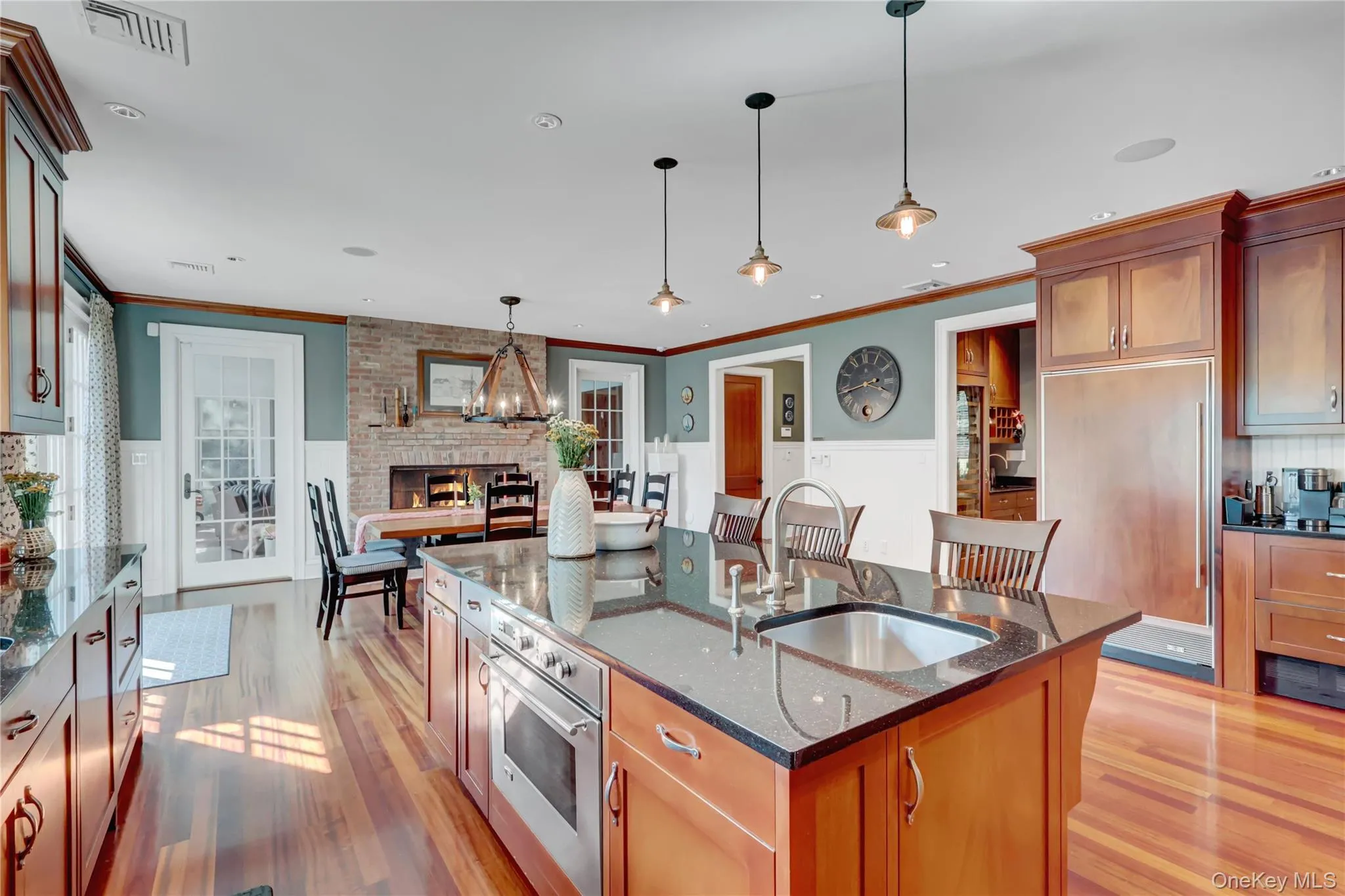Kitchen with dark stone counters, oven, brown cabinetry, an island with sink, and light wood-style floors Kitchen with dark stone counters, oven, brown cabinetry, an island with sink, and light wood-style floors