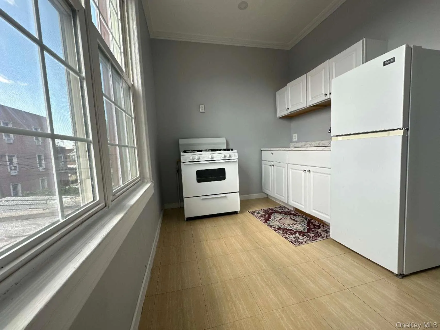 Kitchen with white appliances, plenty of natural light, white cabinetry, crown molding, and light countertops Kitchen with white appliances, plenty of natural light, white cabinetry, crown molding, and light countertops