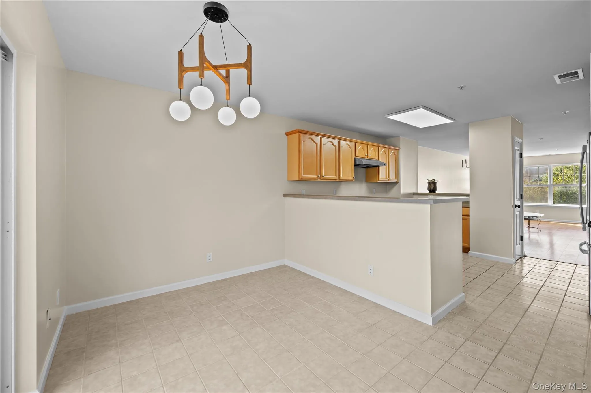 Kitchen featuring a peninsula, light tile patterned floors, a chandelier, under cabinet range hood, and pendant lighting Kitchen featuring a peninsula, light tile patterned floors, a chandelier, under cabinet range hood, and pendant lighting
