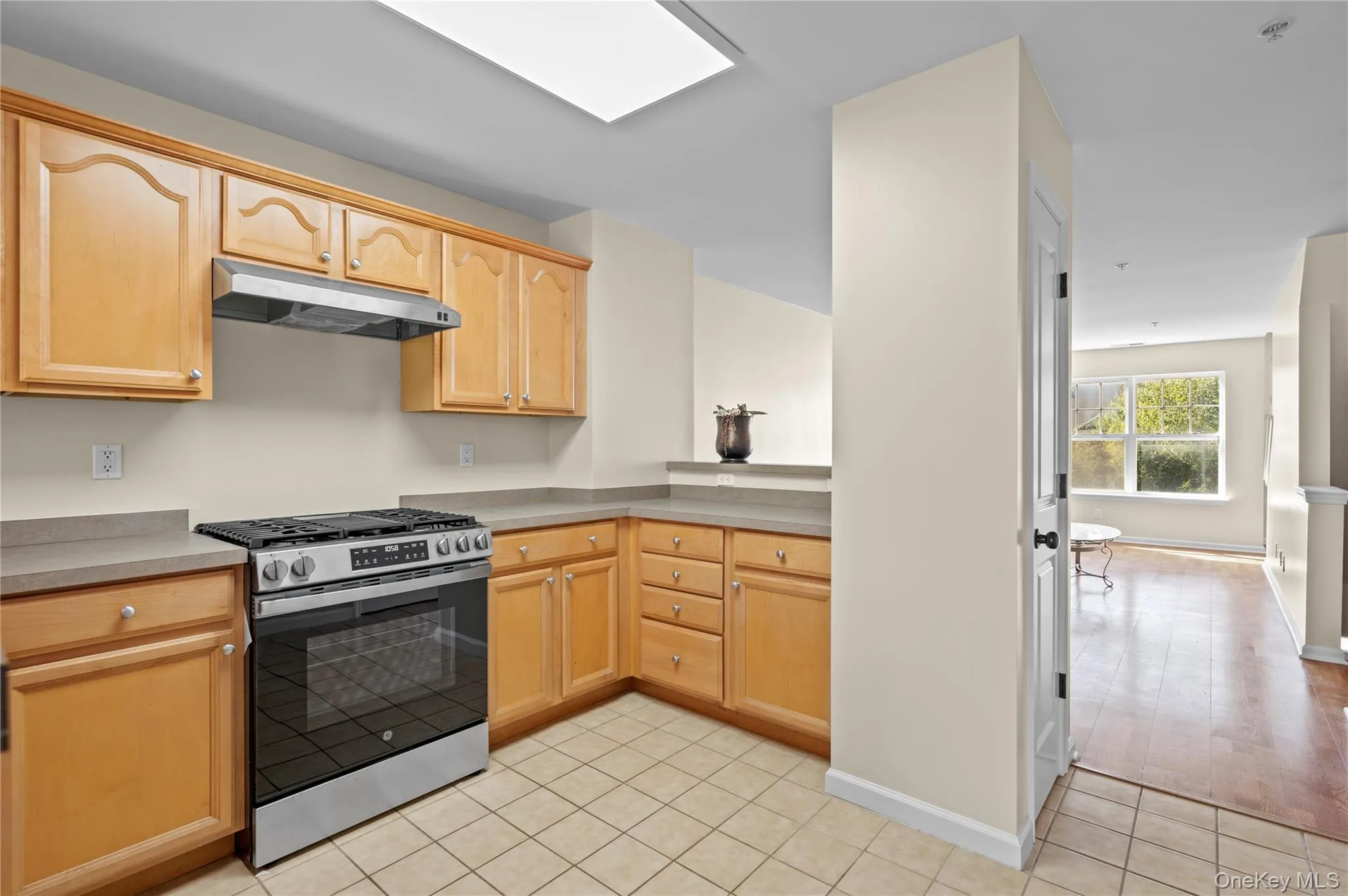 Kitchen featuring gas stove, under cabinet range hood, light brown cabinetry, light tile patterned floors, and a skylight Kitchen featuring gas stove, under cabinet range hood, light brown cabinetry, light tile patterned floors, and a skylight