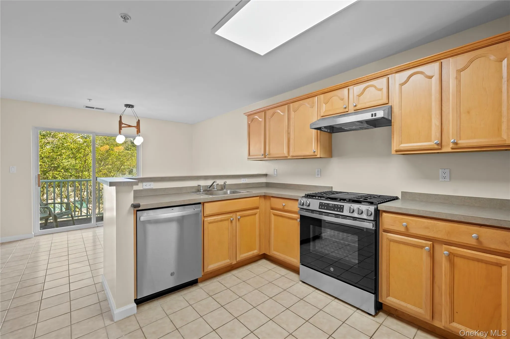Kitchen with a peninsula, appliances with stainless steel finishes, under cabinet range hood, light tile patterned flooring, and hanging light fixtures Kitchen with a peninsula, appliances with stainless steel finishes, under cabinet range hood, light tile patterned flooring, and hanging light fixtures