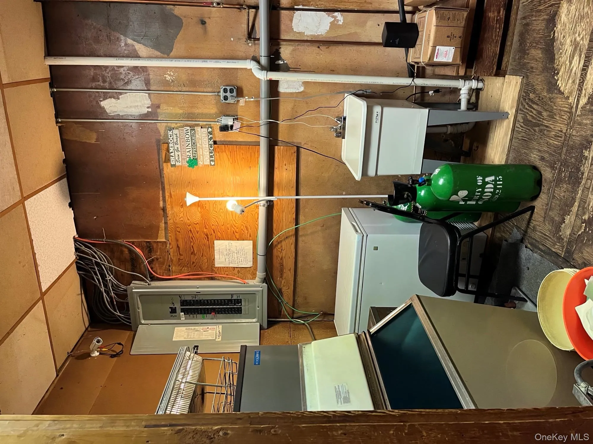 Unfinished below grade area featuring electric panel, fridge, and a paneled ceiling Unfinished below grade area featuring electric panel, fridge, and a paneled ceiling