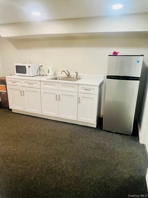 Kitchen with white cabinetry, dark carpet, freestanding refrigerator, and white microwave Kitchen with white cabinetry, dark carpet, freestanding refrigerator, and white microwave