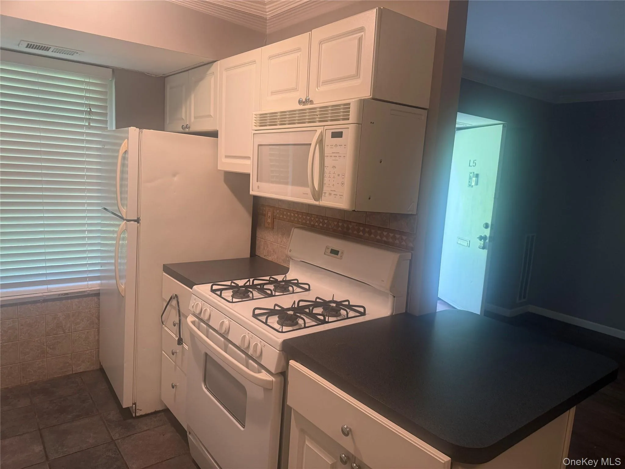 Kitchen featuring dark countertops, white appliances, white cabinetry, and crown molding Kitchen featuring dark countertops, white appliances, white cabinetry, and crown molding