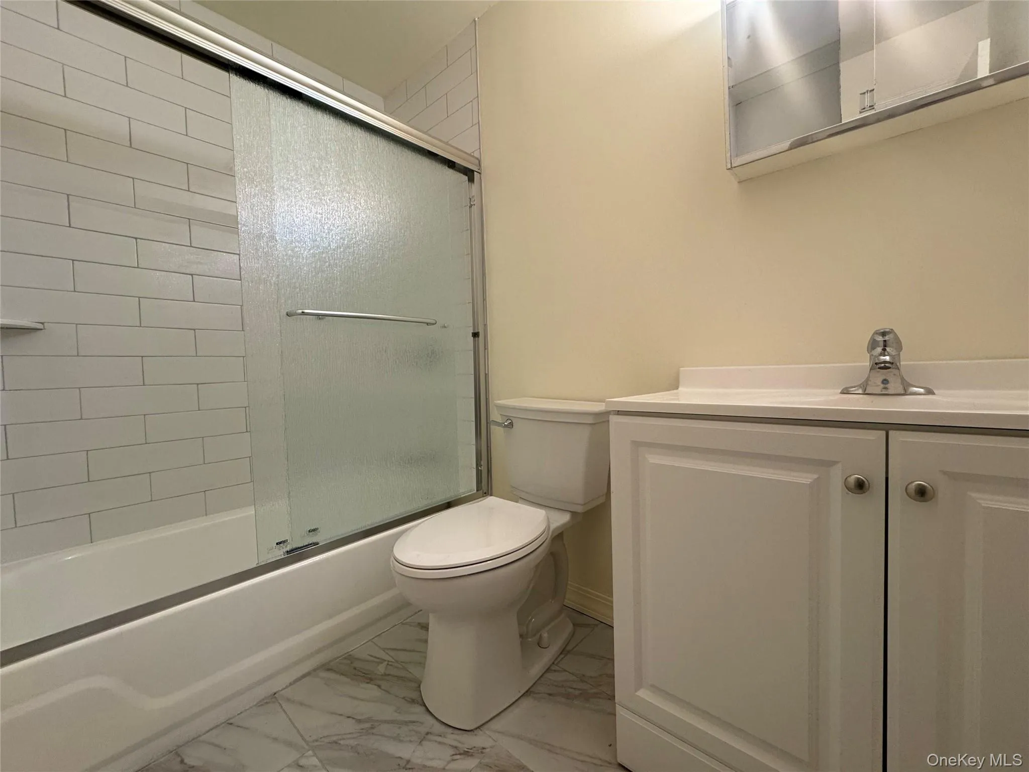 Bathroom featuring combined bath / shower with glass door, vanity, and light marble finish floors Bathroom featuring combined bath / shower with glass door, vanity, and light marble finish floors