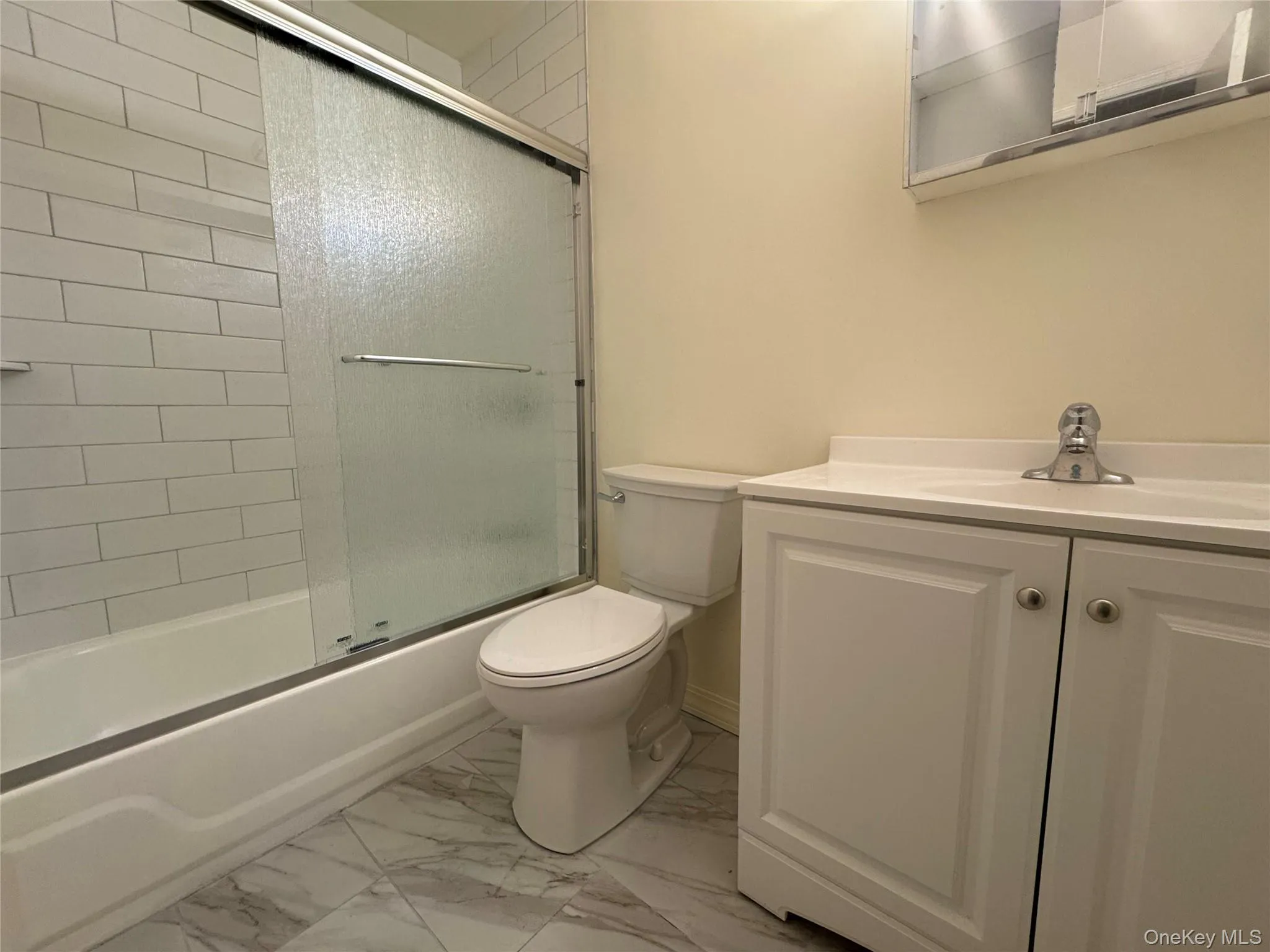 Full bath with enclosed tub / shower combo, vanity, and light marble finish floors Full bath with enclosed tub / shower combo, vanity, and light marble finish floors