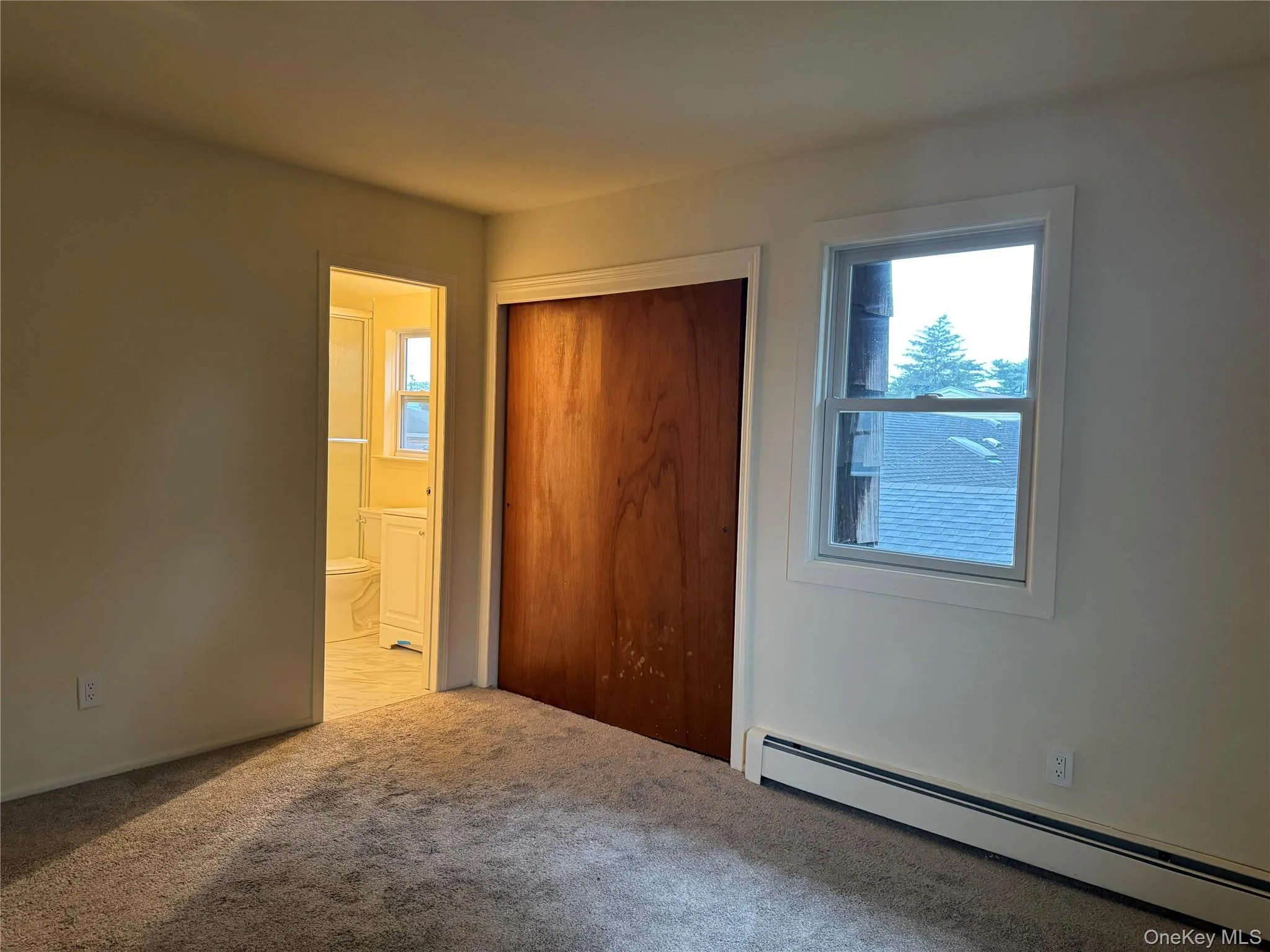 Unfurnished bedroom with baseboard heating, carpet floors, a closet, and connected bathroom Unfurnished bedroom with baseboard heating, carpet floors, a closet, and connected bathroom