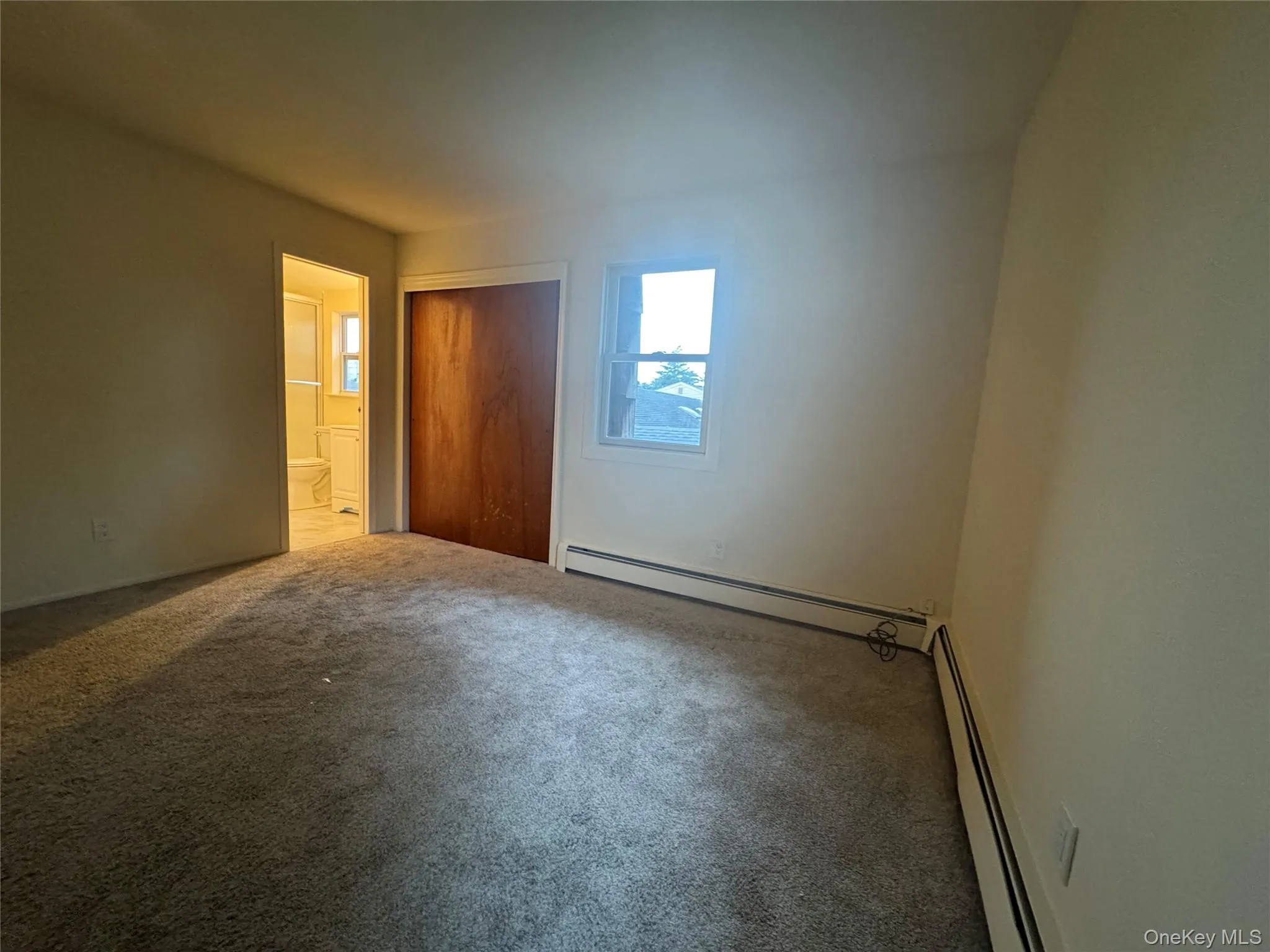 Unfurnished bedroom featuring a baseboard radiator, carpet flooring, and a closet Unfurnished bedroom featuring a baseboard radiator, carpet flooring, and a closet