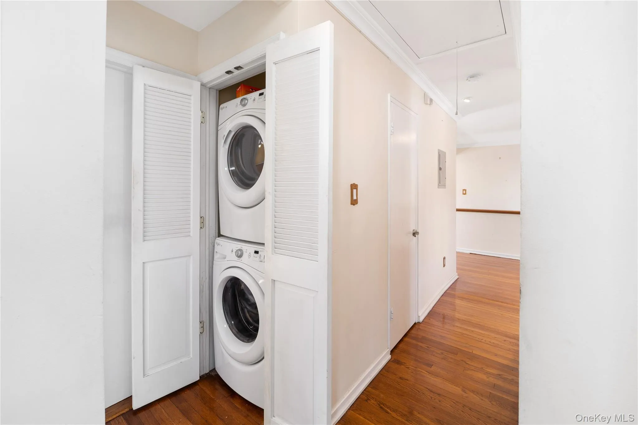Laundry room with attic access, dark wood-style flooring, estacked washer and dryer, and crown molding Laundry room with attic access, dark wood-style flooring, estacked washer and dryer, and crown molding