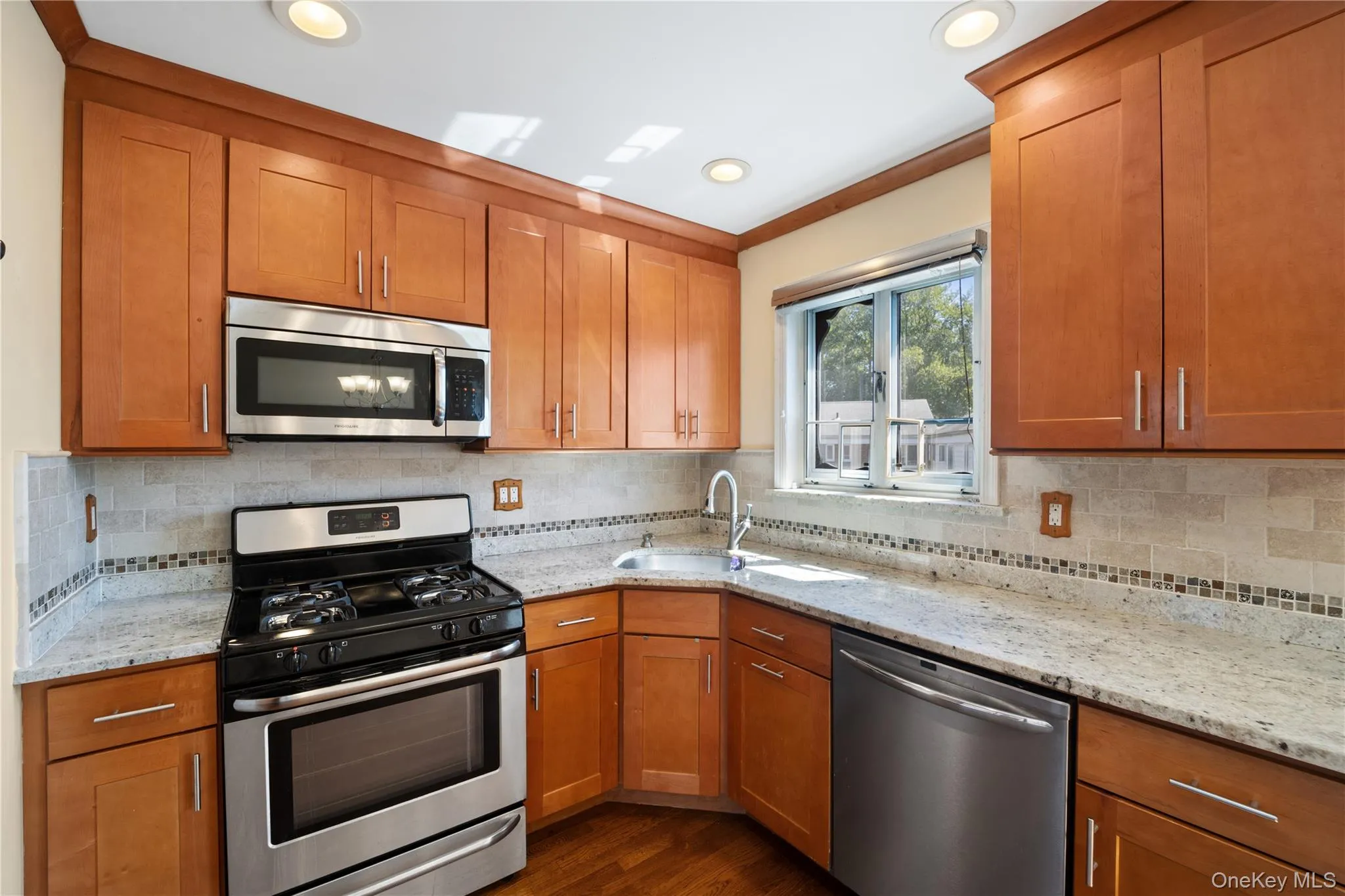 Kitchen featuring stainless steel appliances, brown cabinetry, light stone counters, decorative backsplash, and recessed lighting Kitchen featuring stainless steel appliances, brown cabinetry, light stone counters, decorative backsplash, and recessed lighting