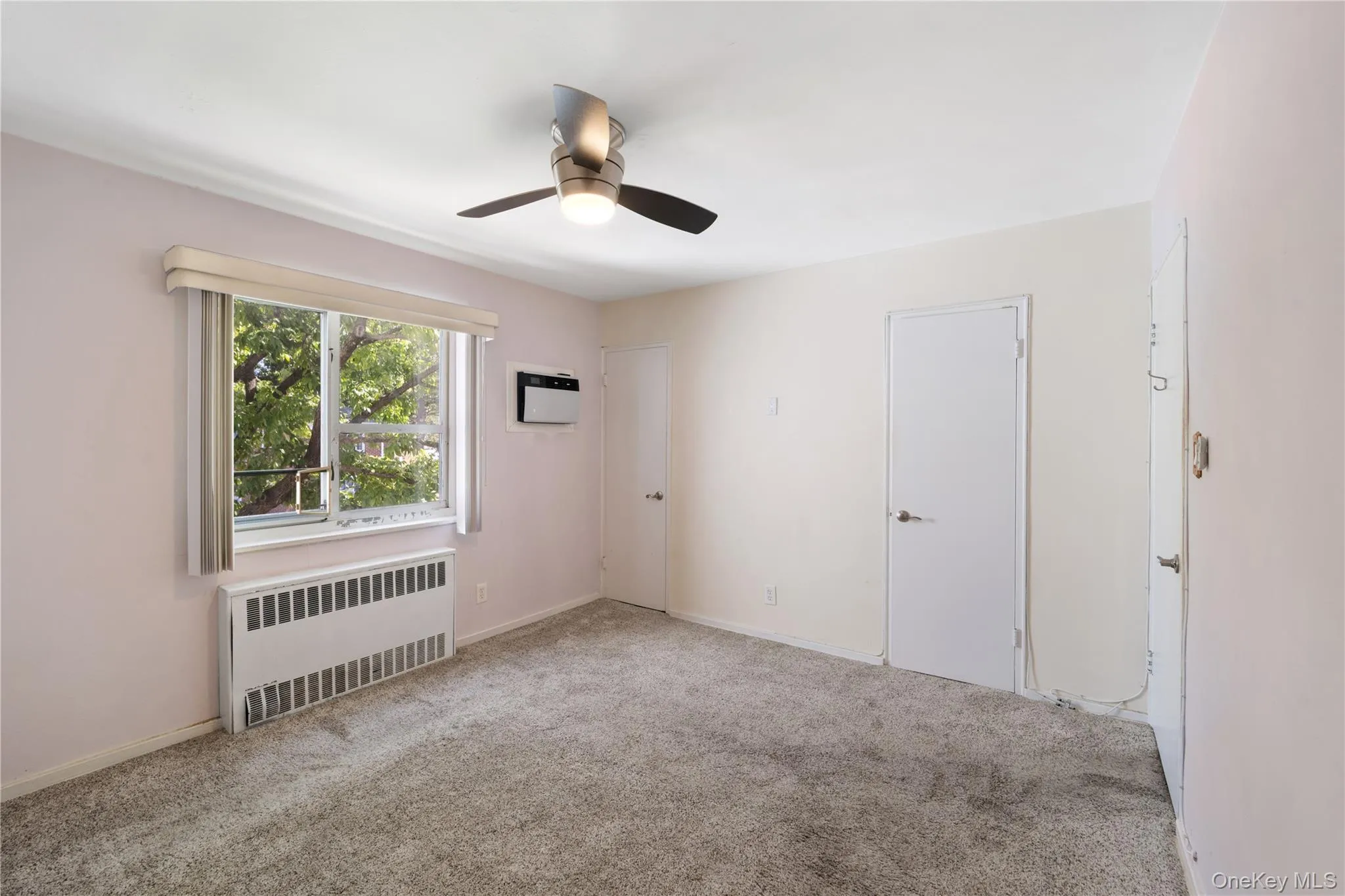 Carpeted spare room featuring radiator and a ceiling fan Carpeted spare room featuring radiator and a ceiling fan