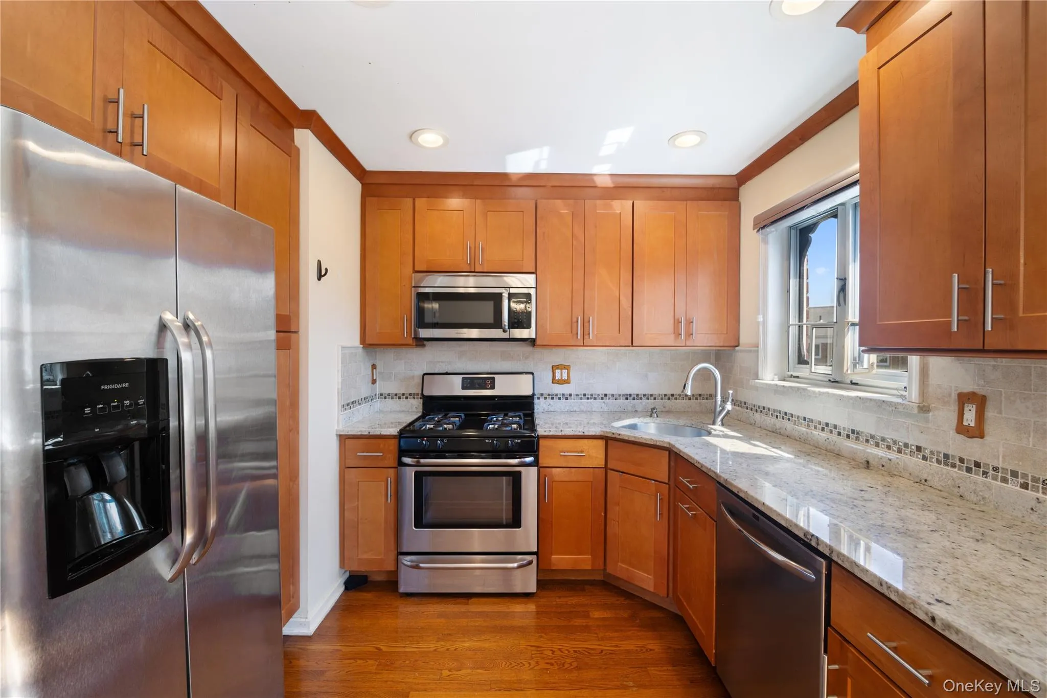 Kitchen featuring stainless steel appliances, brown cabinetry, light stone countertops, tasteful backsplash, and recessed lighting Kitchen featuring stainless steel appliances, brown cabinetry, light stone countertops, tasteful backsplash, and recessed lighting