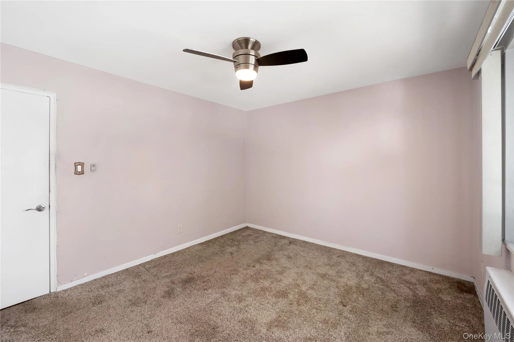 Empty room with carpet, radiator heating unit, and ceiling fan Empty room with carpet, radiator heating unit, and ceiling fan
