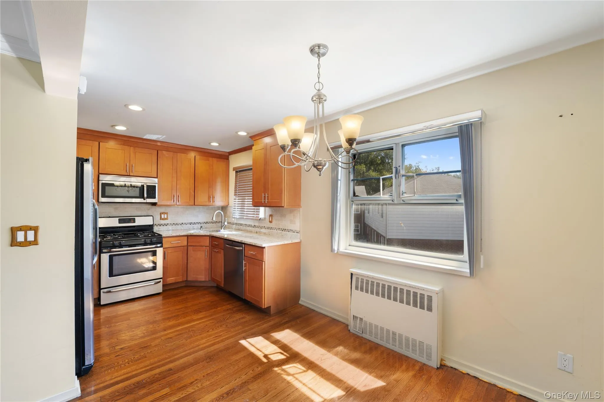Kitchen with a chandelier, radiator, stainless steel appliances, brown cabinets, and dark wood-style floors Kitchen with a chandelier, radiator, stainless steel appliances, brown cabinets, and dark wood-style floors