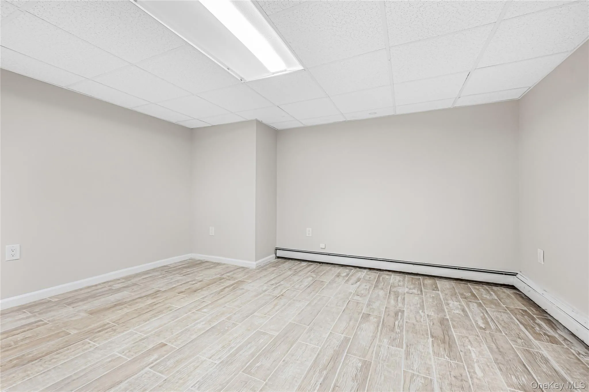 Unfurnished room with a baseboard heating unit, baseboard heating, wood tiled floors, and a drop ceiling Unfurnished room with a baseboard heating unit, baseboard heating, wood tiled floors, and a drop ceiling