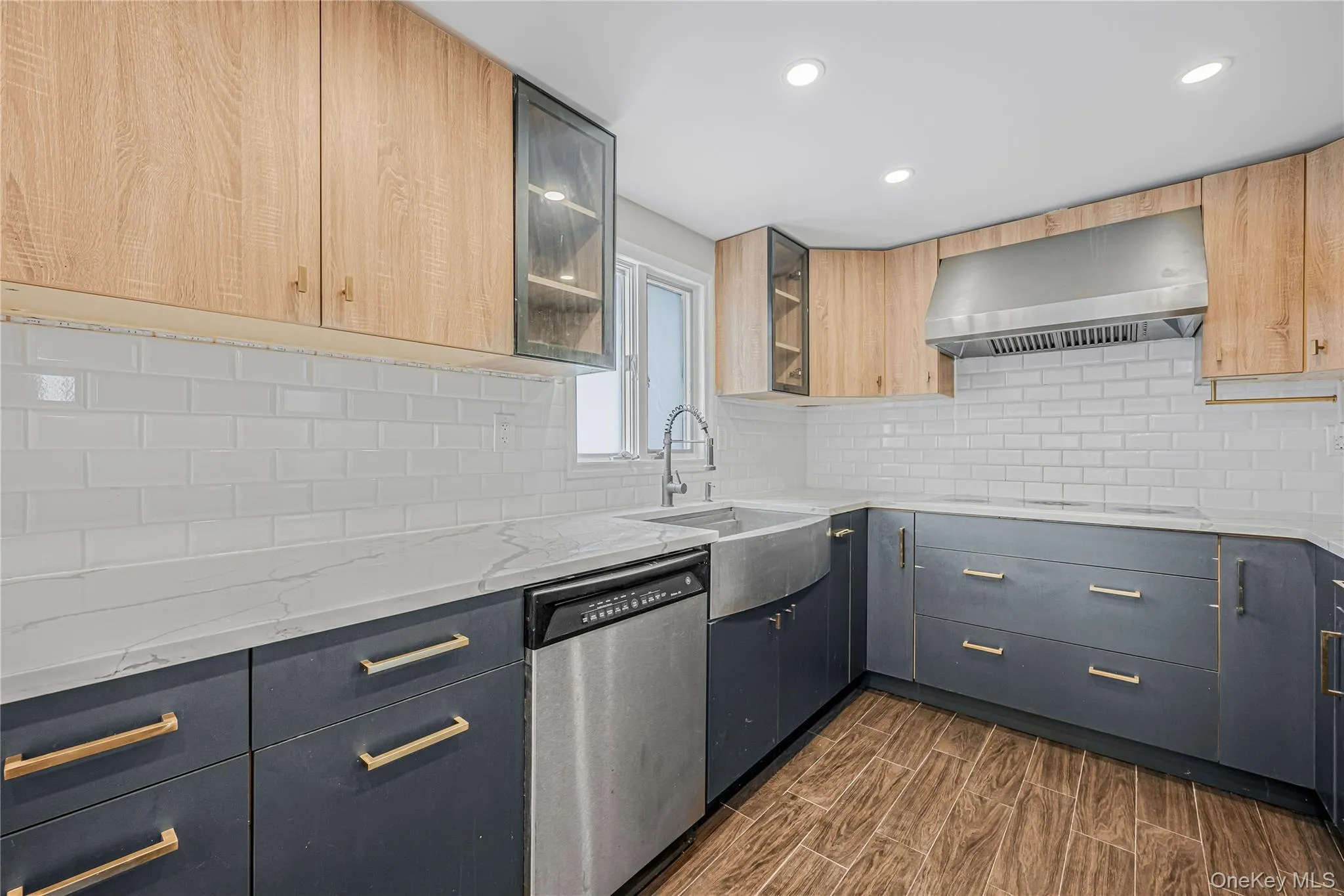 Kitchen featuring light stone countertops, dishwasher, decorative backsplash, wood finish floors, and wall chimney exhaust hood Kitchen featuring light stone countertops, dishwasher, decorative backsplash, wood finish floors, and wall chimney exhaust hood