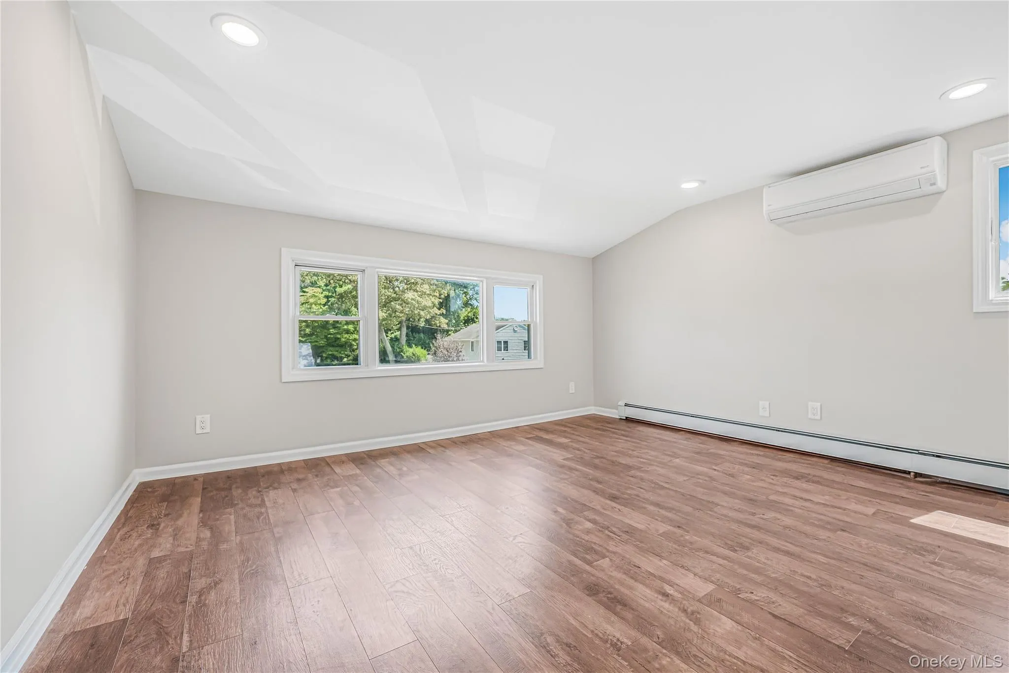 Spare room featuring recessed lighting, light wood-style flooring, an AC wall unit, and a baseboard heating unit Spare room featuring recessed lighting, light wood-style flooring, an AC wall unit, and a baseboard heating unit