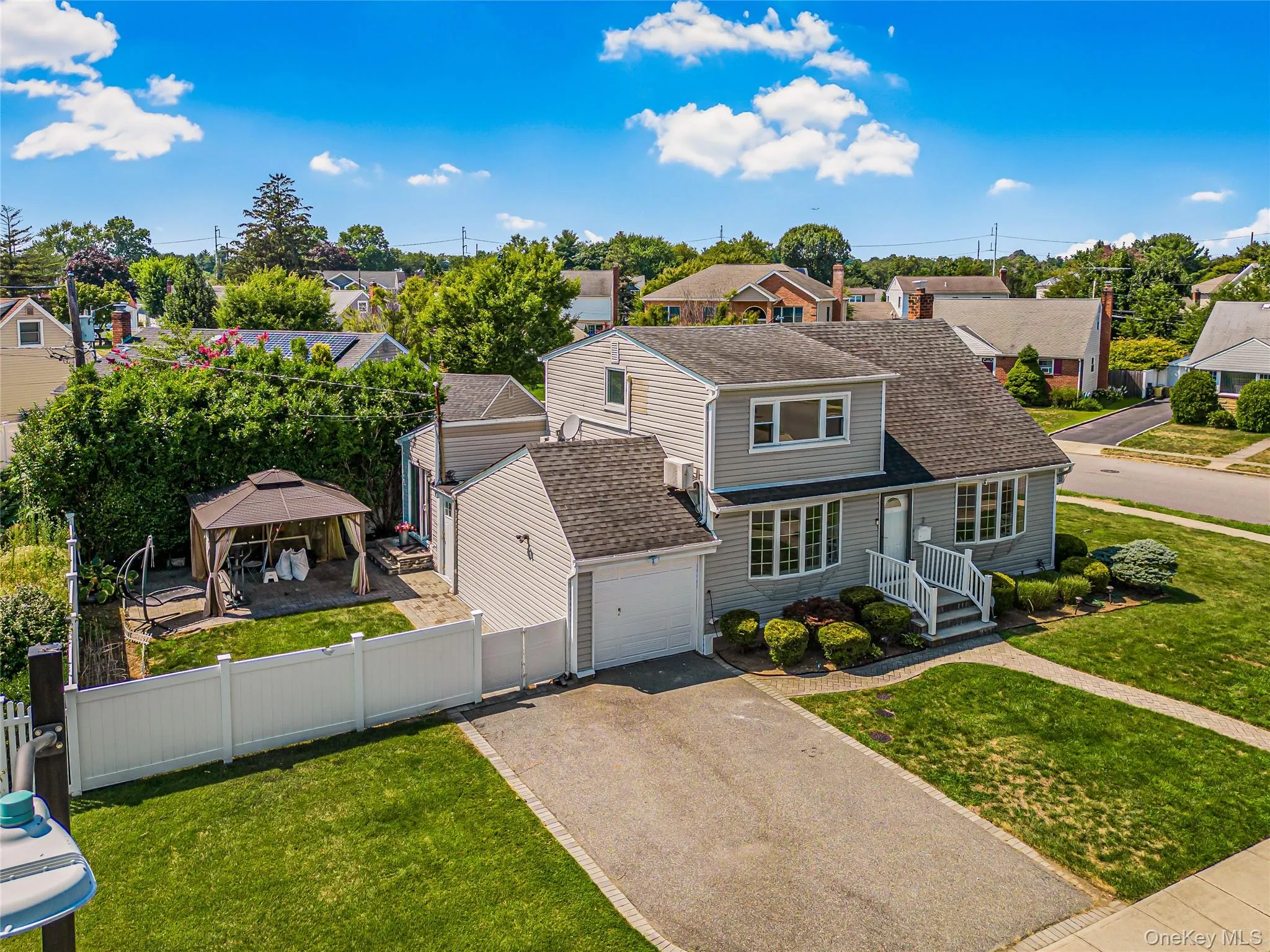 Traditional-style house with a residential view, roof with shingles, asphalt driveway, a gazebo, and an attached garage Traditional-style house with a residential view, roof with shingles, asphalt driveway, a gazebo, and an attached garage
