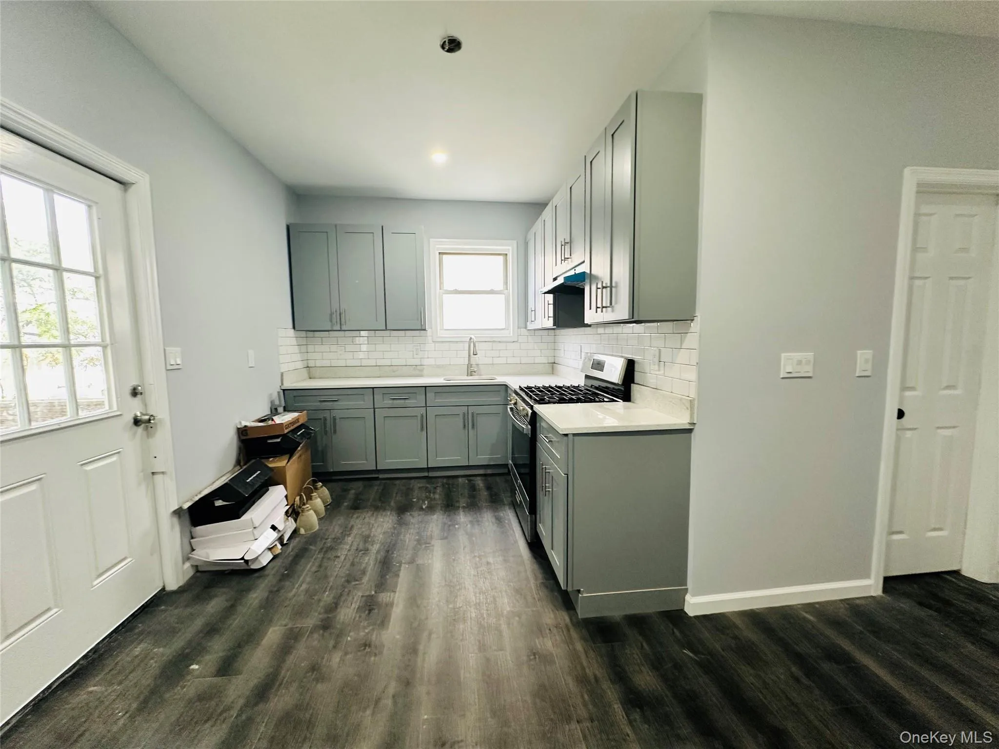 Kitchen featuring stainless steel gas range oven, dark wood-style flooring, decorative backsplash, gray cabinetry, and light stone counters Kitchen featuring stainless steel gas range oven, dark wood-style flooring, decorative backsplash, gray cabinetry, and light stone counters