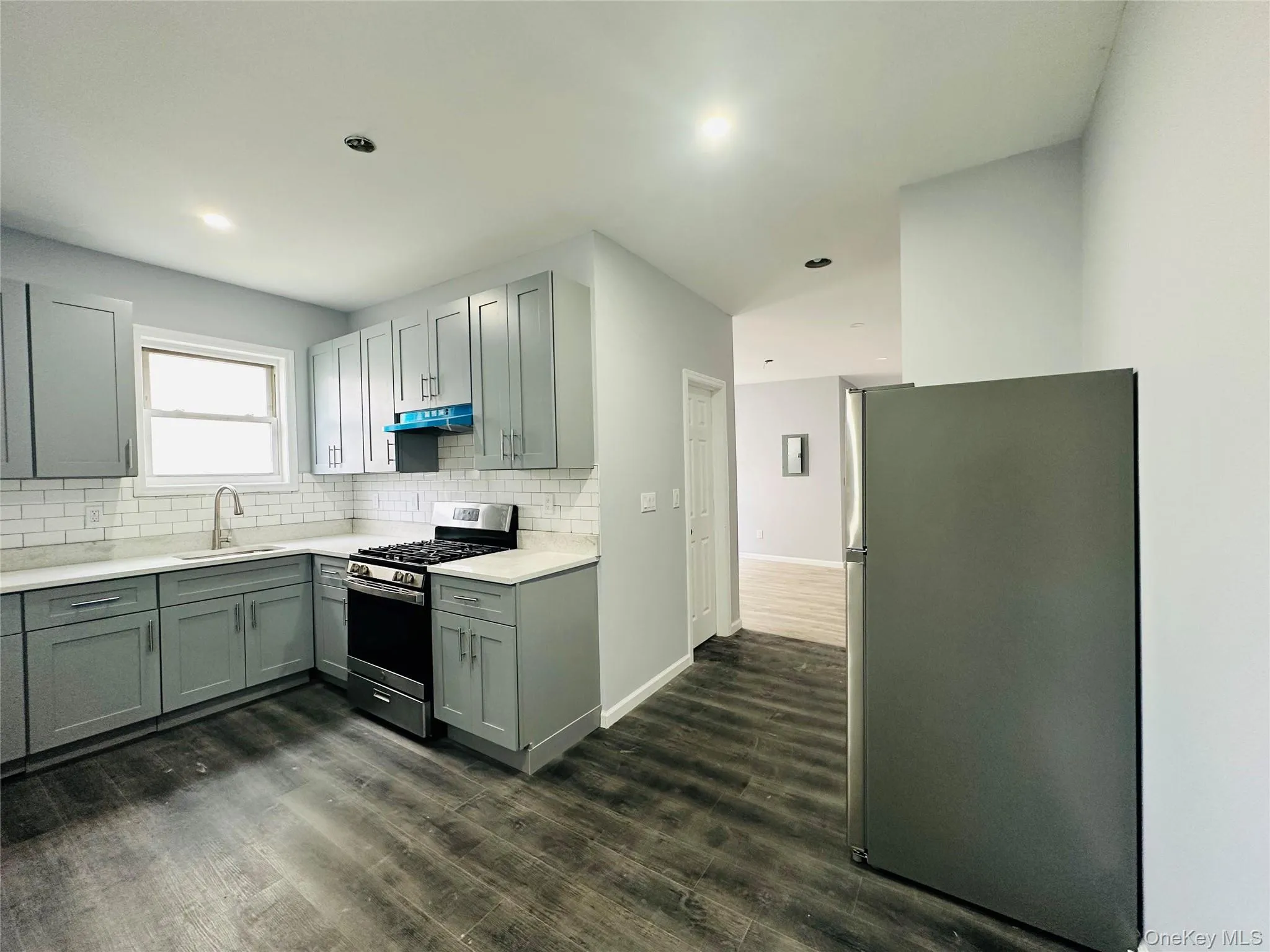 Kitchen with stainless steel appliances, decorative backsplash, gray cabinetry, dark wood finished floors, and light stone counters Kitchen with stainless steel appliances, decorative backsplash, gray cabinetry, dark wood finished floors, and light stone counters
