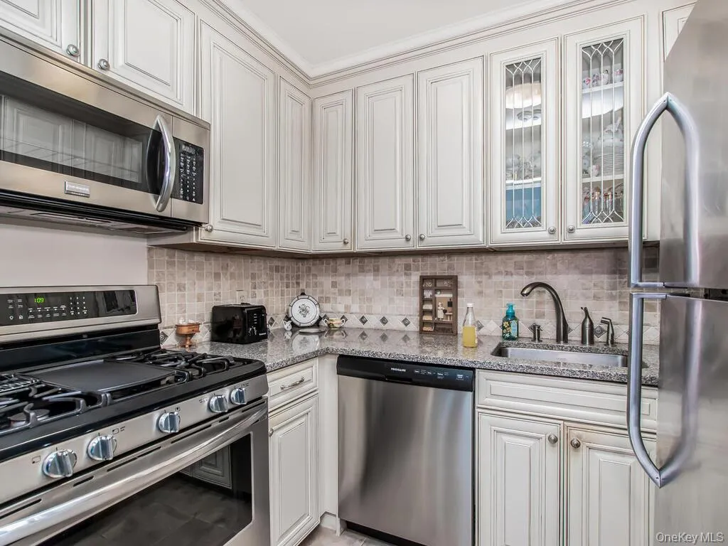 Kitchen featuring stainless steel appliances, light stone counters, and white cabinetry Kitchen featuring stainless steel appliances, light stone counters, and white cabinetry