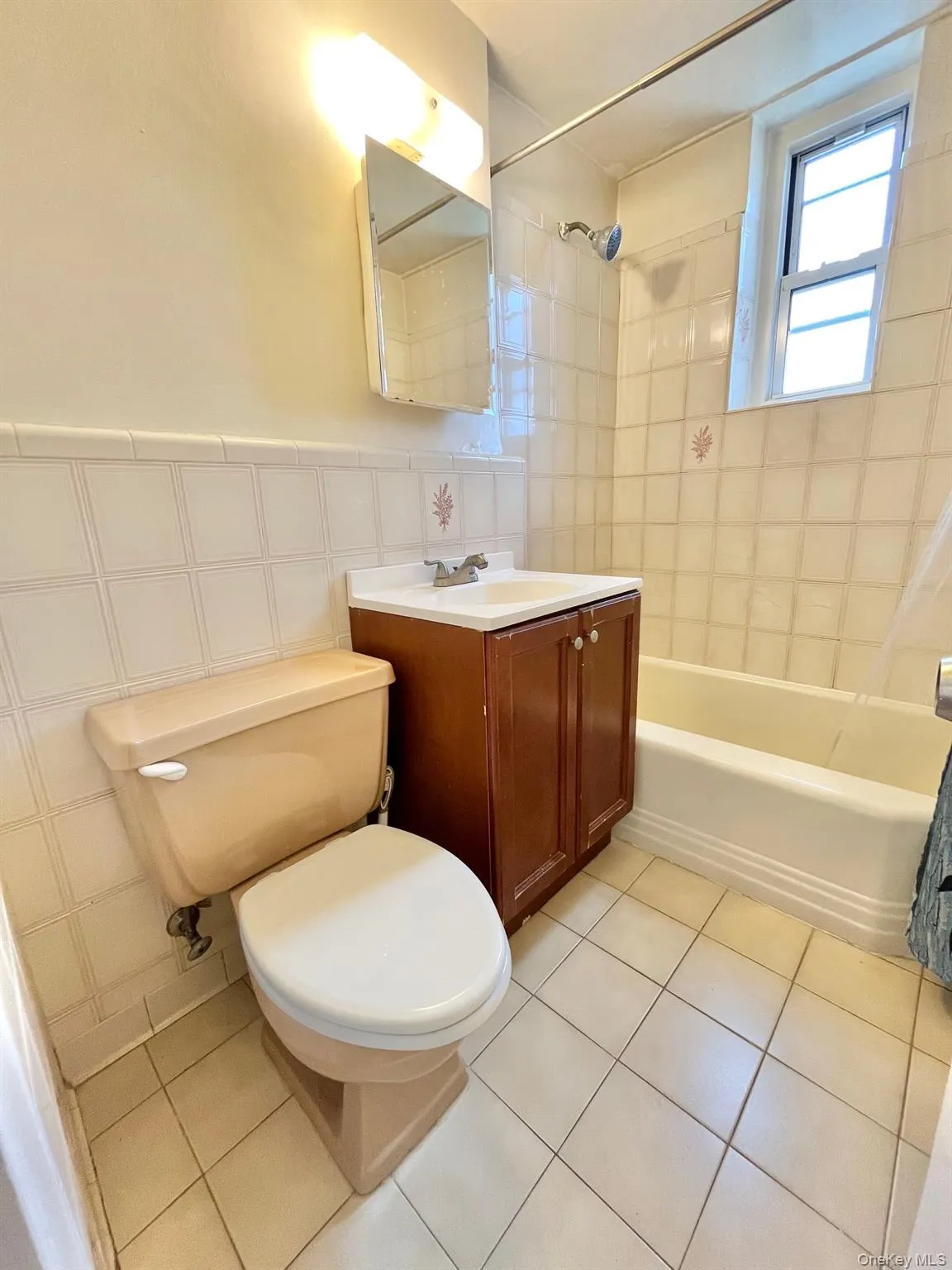Full bath featuring shower / bath combo, vanity, light tile patterned flooring, tile walls, and wainscoting Full bath featuring shower / bath combo, vanity, light tile patterned flooring, tile walls, and wainscoting