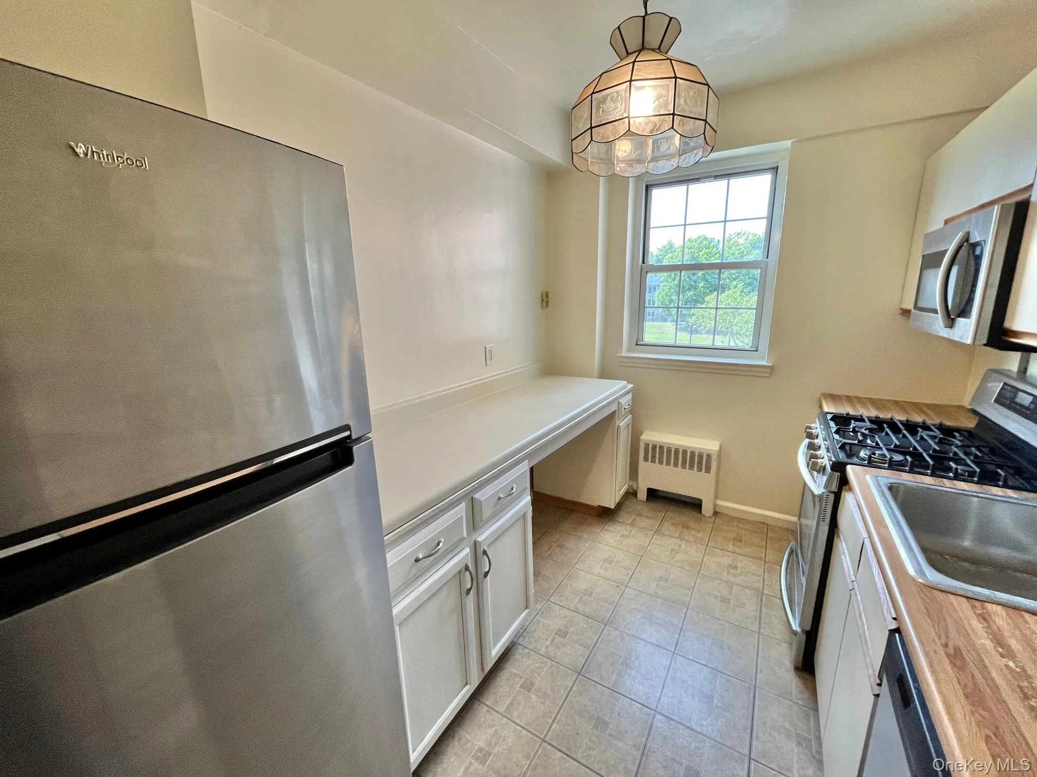 Kitchen featuring white cabinets, stainless steel appliances, light countertops, decorative light fixtures, and radiator heating unit Kitchen featuring white cabinets, stainless steel appliances, light countertops, decorative light fixtures, and radiator heating unit