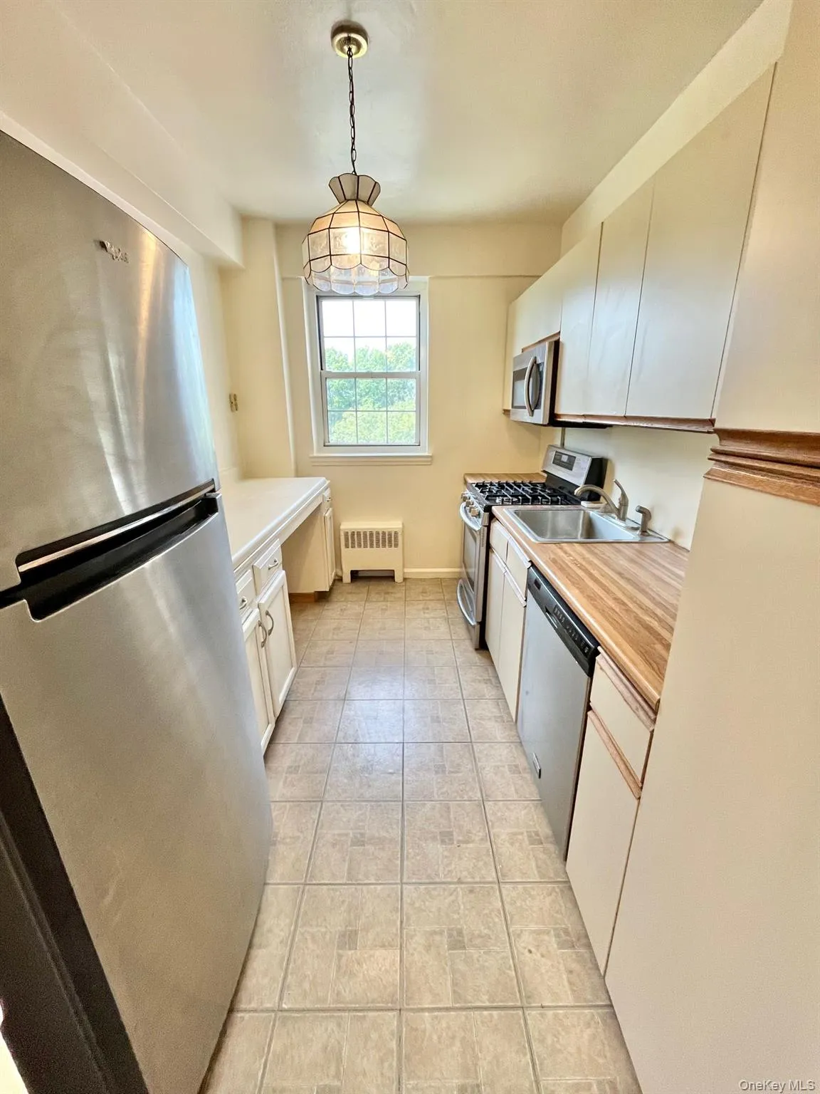 Kitchen featuring stainless steel appliances, light countertops, decorative light fixtures, white cabinetry, and radiator Kitchen featuring stainless steel appliances, light countertops, decorative light fixtures, white cabinetry, and radiator
