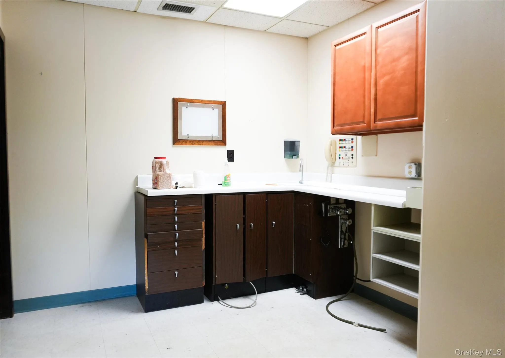 Kitchen with a drop ceiling, light countertops, light flooring, and dark brown cabinetry Kitchen with a drop ceiling, light countertops, light flooring, and dark brown cabinetry