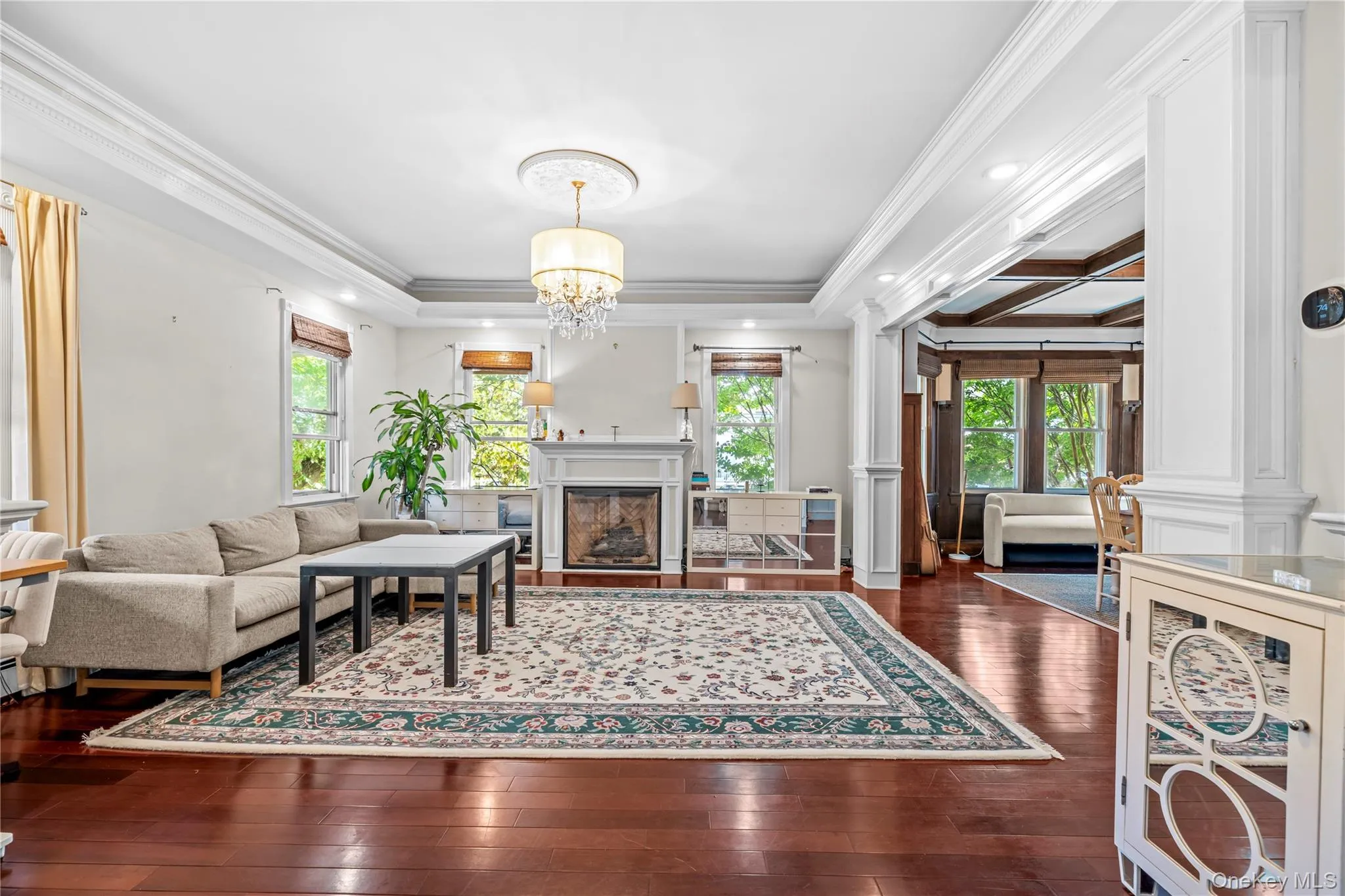 Living area with a fireplace, crown molding, dark wood-style floors, decorative columns, and a chandelier Living area with a fireplace, crown molding, dark wood-style floors, decorative columns, and a chandelier