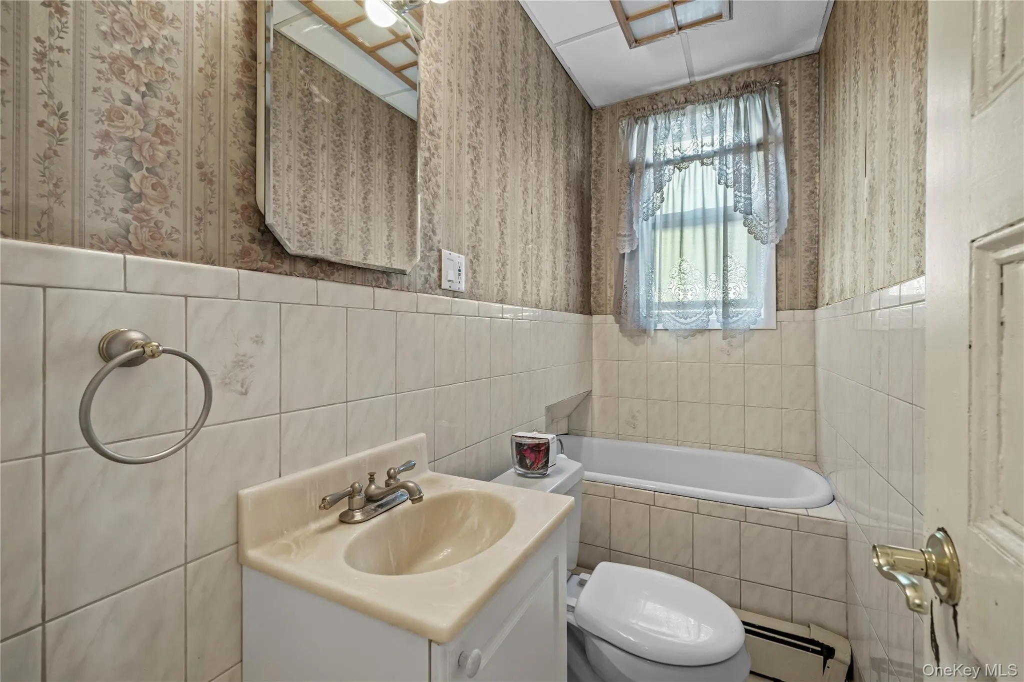 Bathroom with wallpapered walls, vanity, baseboard heating, wainscoting, and tiled tub Bathroom with wallpapered walls, vanity, baseboard heating, wainscoting, and tiled tub