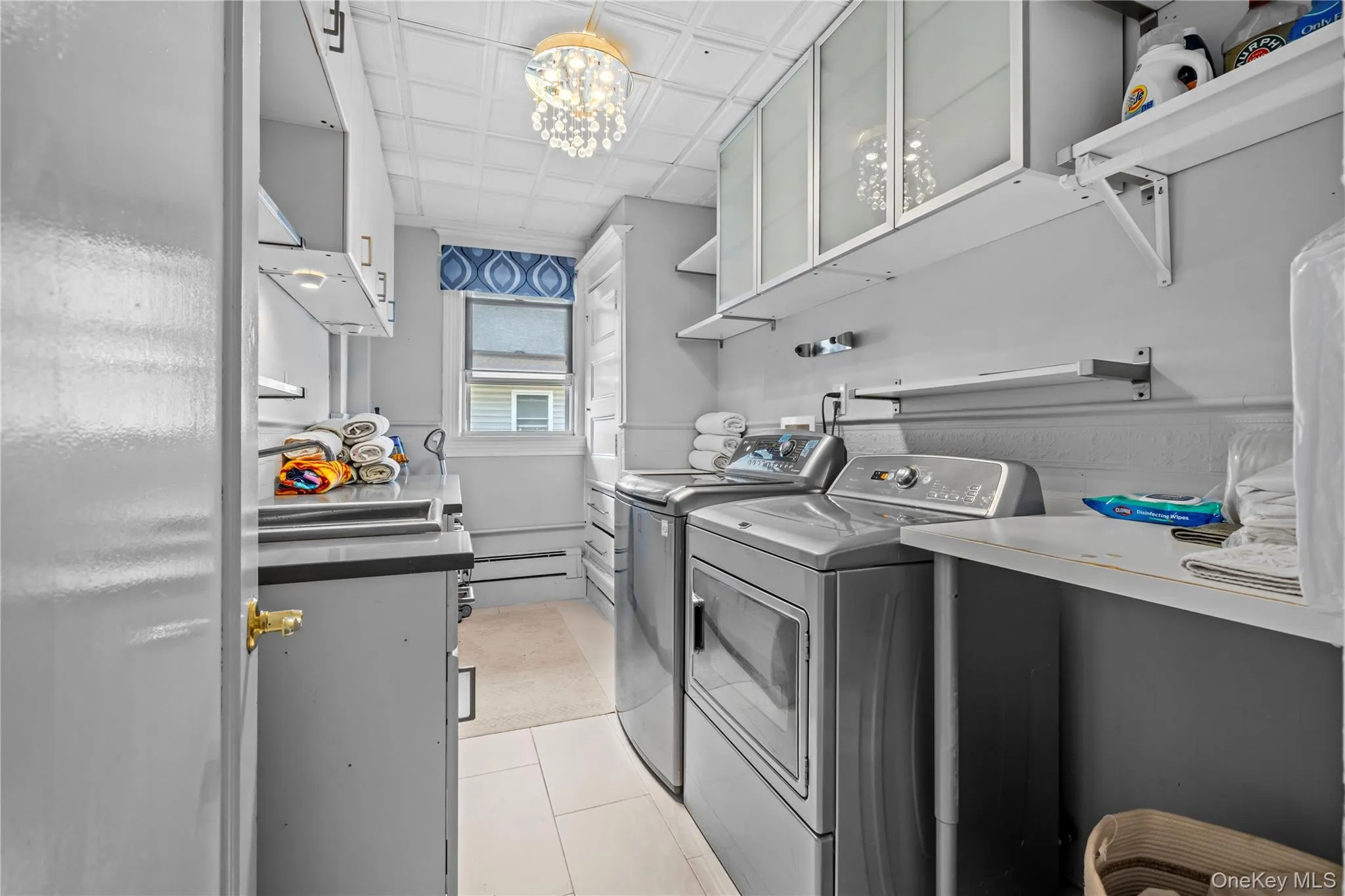 Laundry room with light tile patterned floors, a chandelier, washer and clothes dryer, an ornate ceiling, and baseboard heating Laundry room with light tile patterned floors, a chandelier, washer and clothes dryer, an ornate ceiling, and baseboard heating