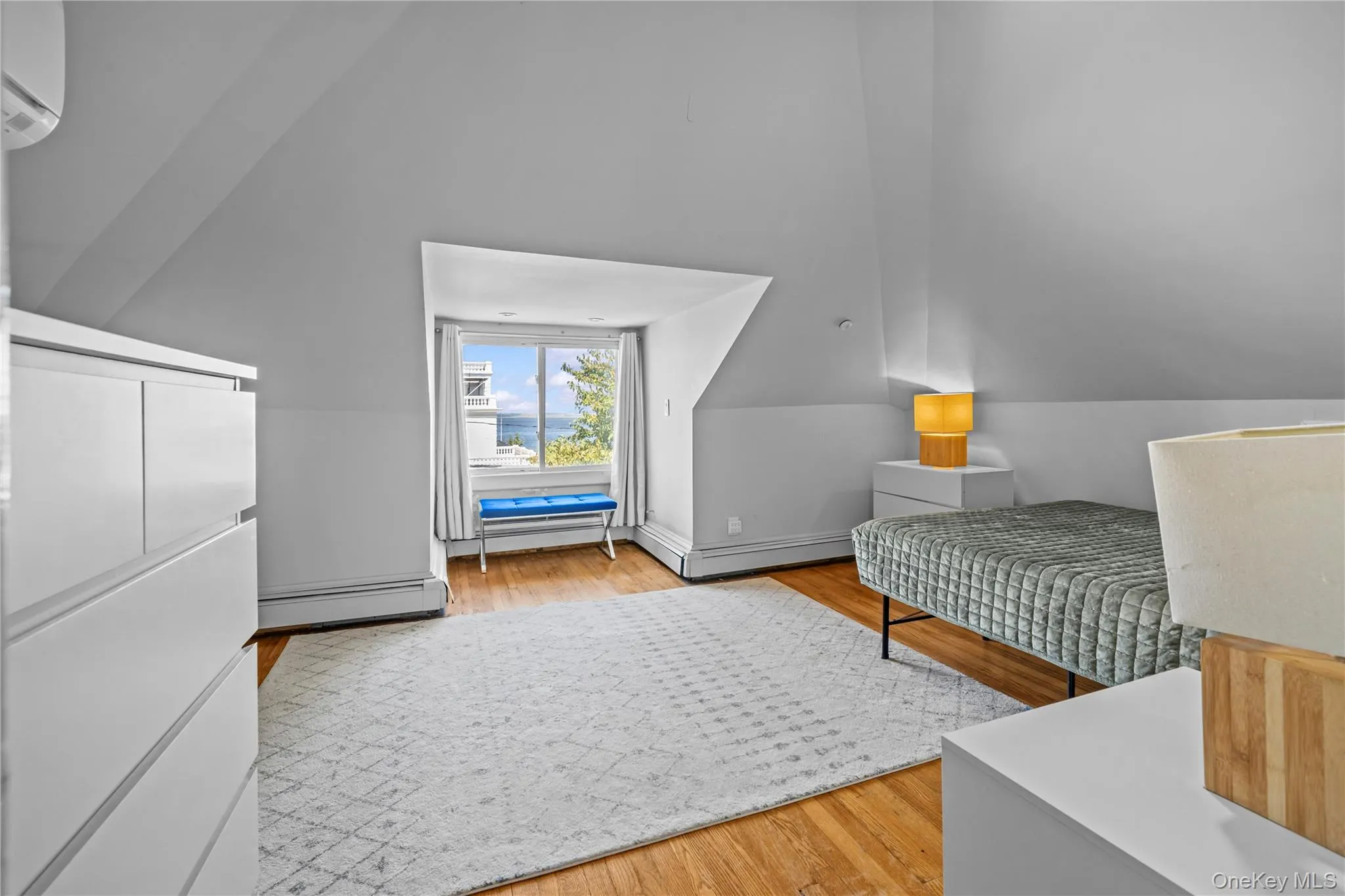 Bedroom with light wood-type flooring, baseboard heating, an AC wall unit, and lofted ceiling Bedroom with light wood-type flooring, baseboard heating, an AC wall unit, and lofted ceiling
