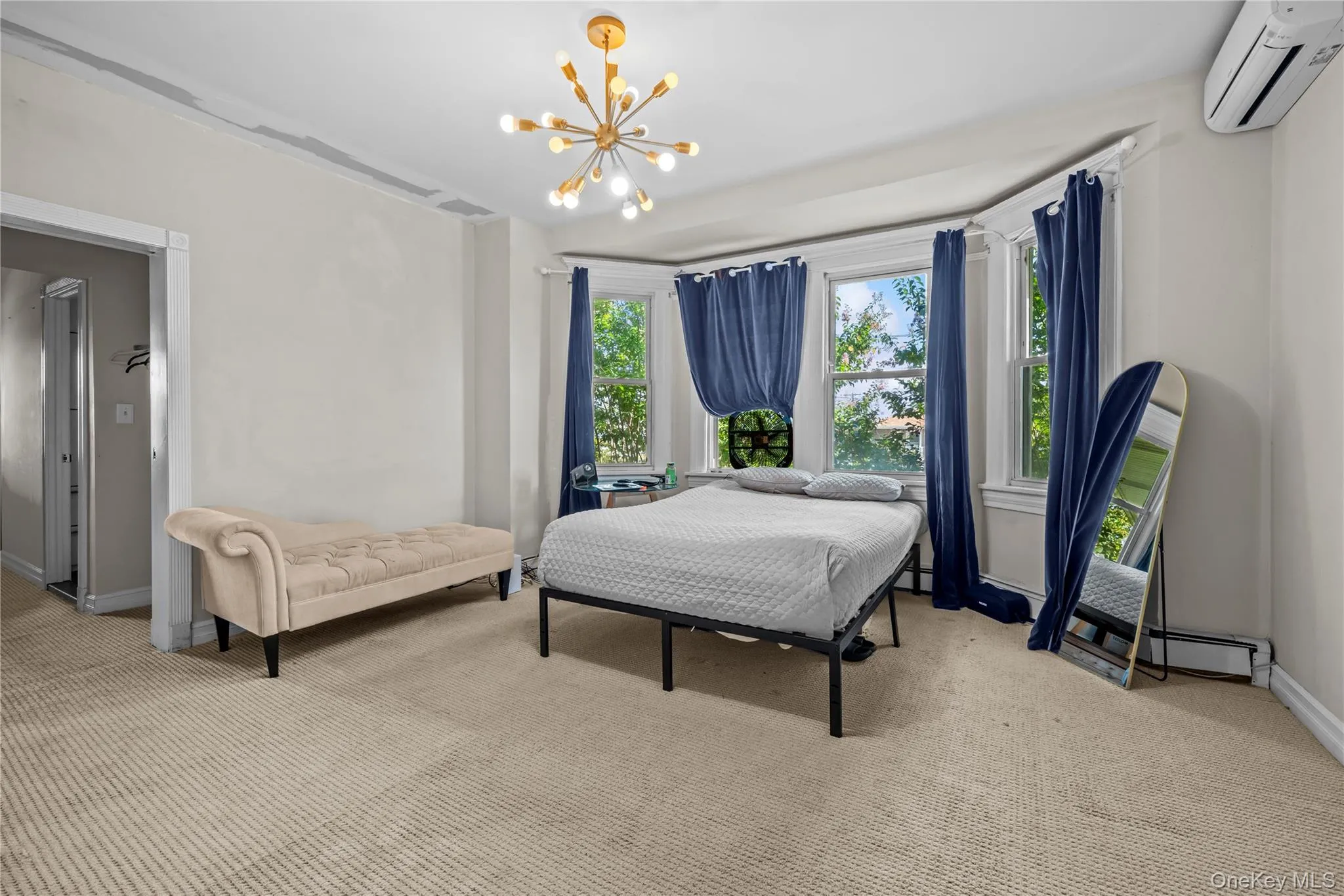 Carpeted bedroom featuring a chandelier, a wall mounted AC, and a baseboard heating unit Carpeted bedroom featuring a chandelier, a wall mounted AC, and a baseboard heating unit