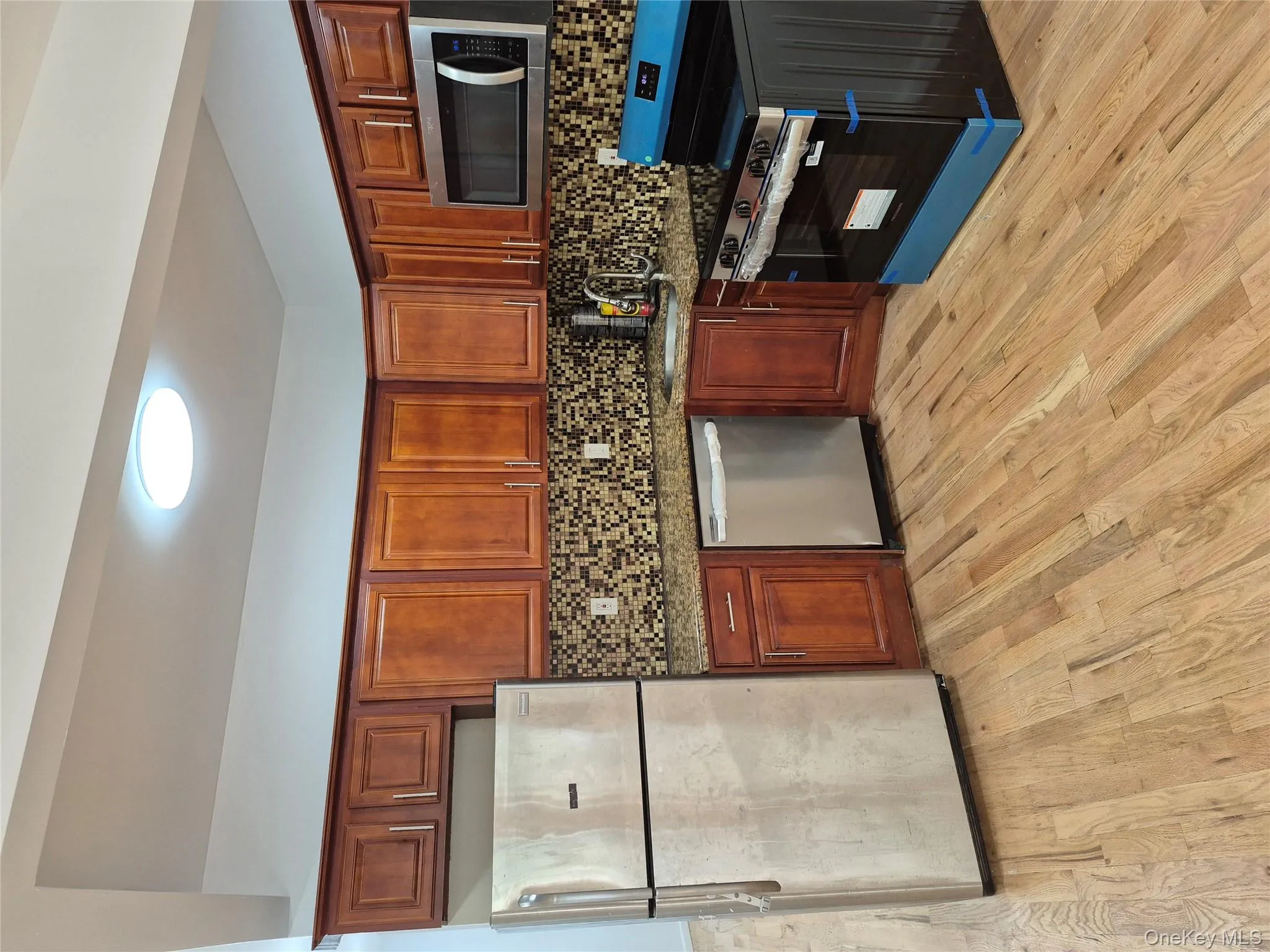 Kitchen featuring appliances with stainless steel finishes, dark stone countertops, decorative backsplash, and light wood finished floors Kitchen featuring appliances with stainless steel finishes, dark stone countertops, decorative backsplash, and light wood finished floors
