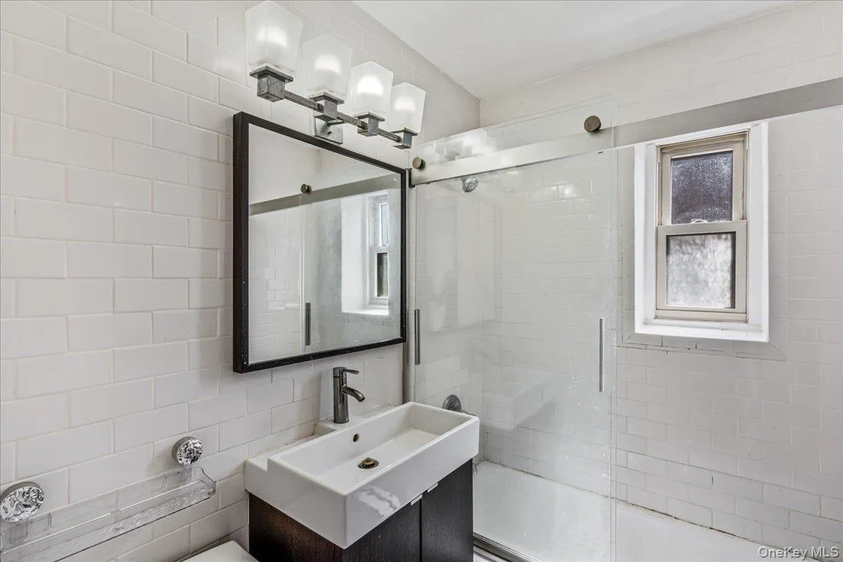Full bathroom with shower / bath combination with glass door, vanity, and tile walls Full bathroom with shower / bath combination with glass door, vanity, and tile walls