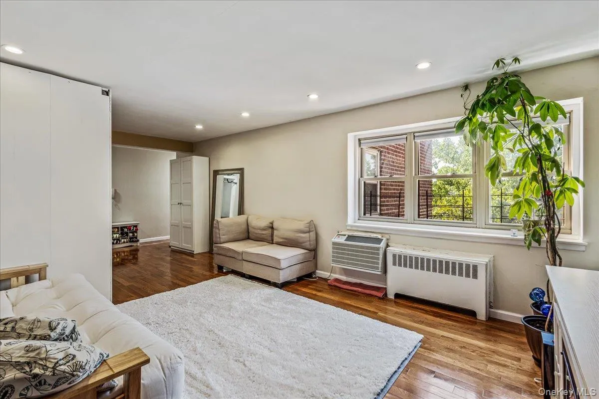 Living room featuring radiator, dark wood-type flooring, recessed lighting, and an AC wall unit Living room featuring radiator, dark wood-type flooring, recessed lighting, and an AC wall unit