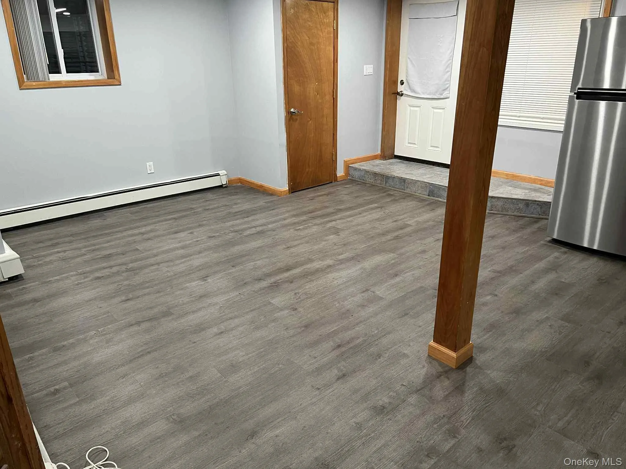 Basement featuring freestanding refrigerator, a baseboard heating unit, and dark wood-style floors Basement featuring freestanding refrigerator, a baseboard heating unit, and dark wood-style floors