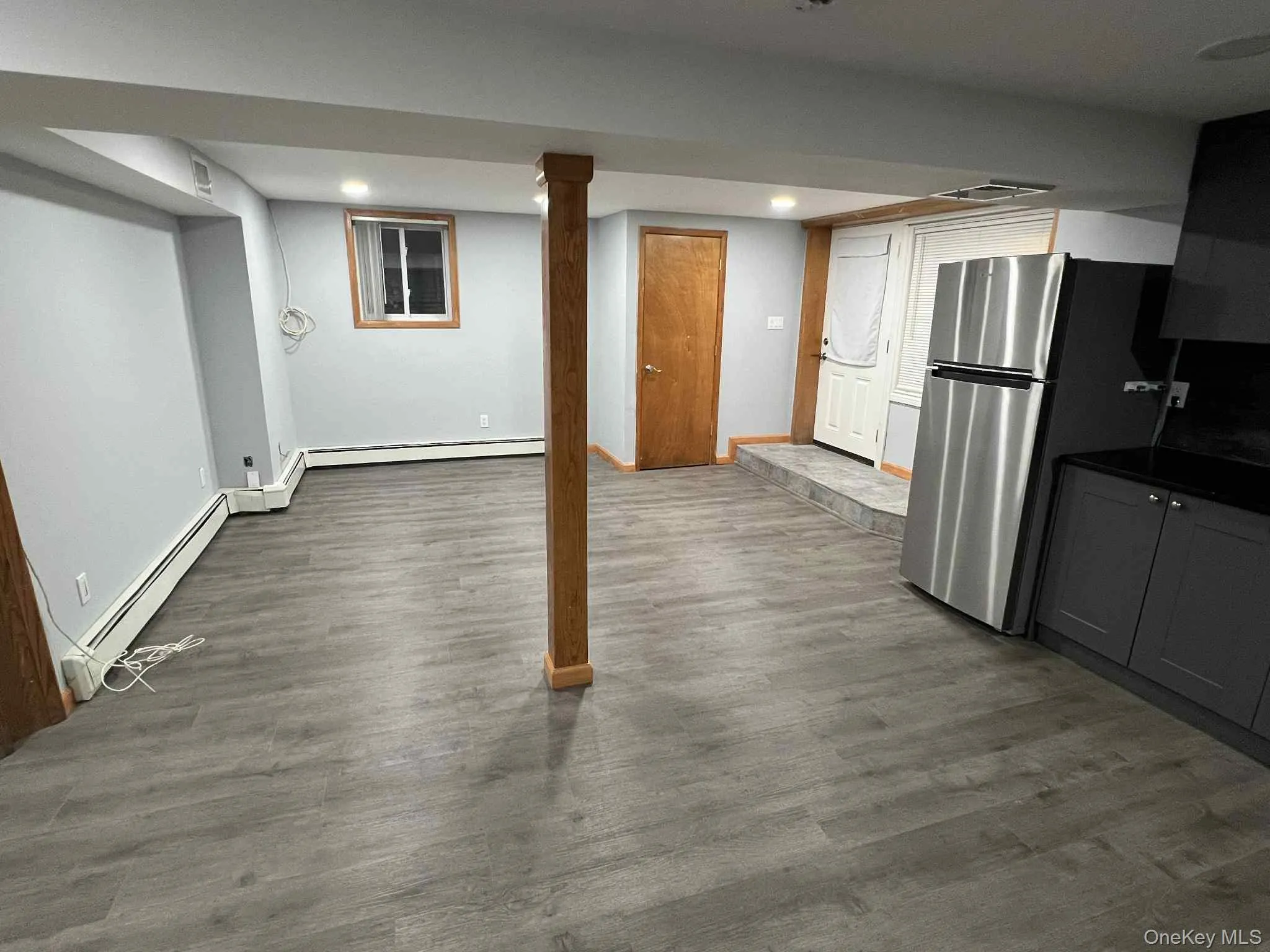 Finished below grade area with freestanding refrigerator, dark wood-style flooring, recessed lighting, and a baseboard heating unit Finished below grade area with freestanding refrigerator, dark wood-style flooring, recessed lighting, and a baseboard heating unit