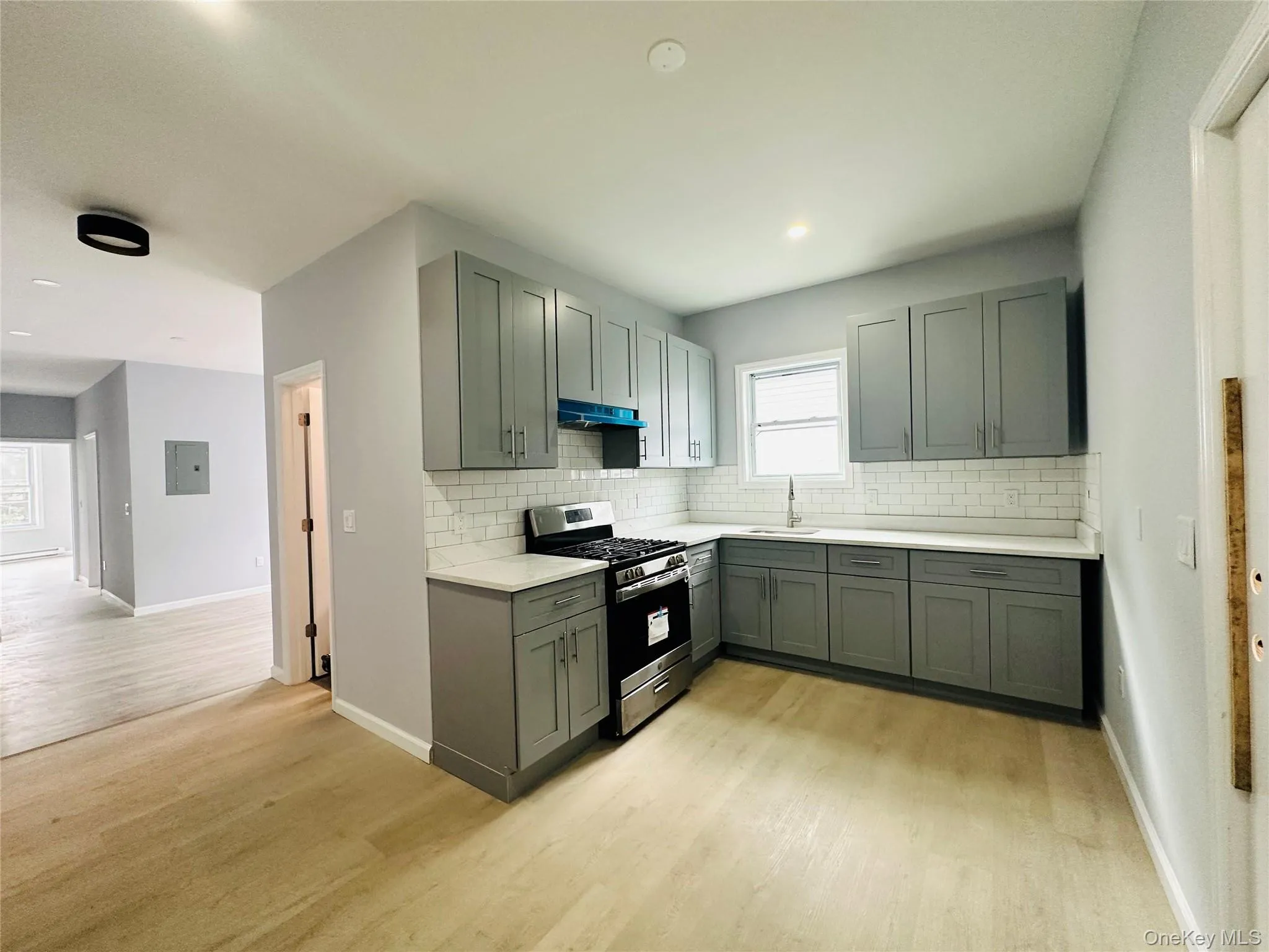Kitchen featuring stainless steel gas range oven, light wood-style flooring, decorative backsplash, and gray cabinets Kitchen featuring stainless steel gas range oven, light wood-style flooring, decorative backsplash, and gray cabinets