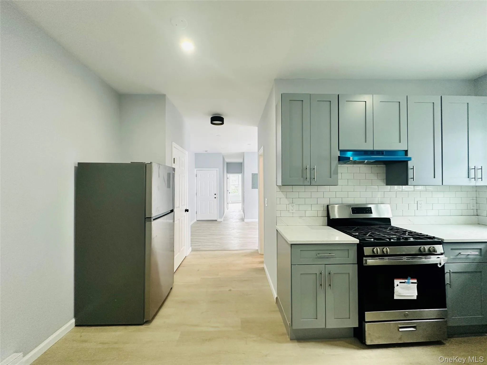 Kitchen with appliances with stainless steel finishes, light wood-style floors, light stone counters, decorative backsplash, and under cabinet range hood Kitchen with appliances with stainless steel finishes, light wood-style floors, light stone counters, decorative backsplash, and under cabinet range hood