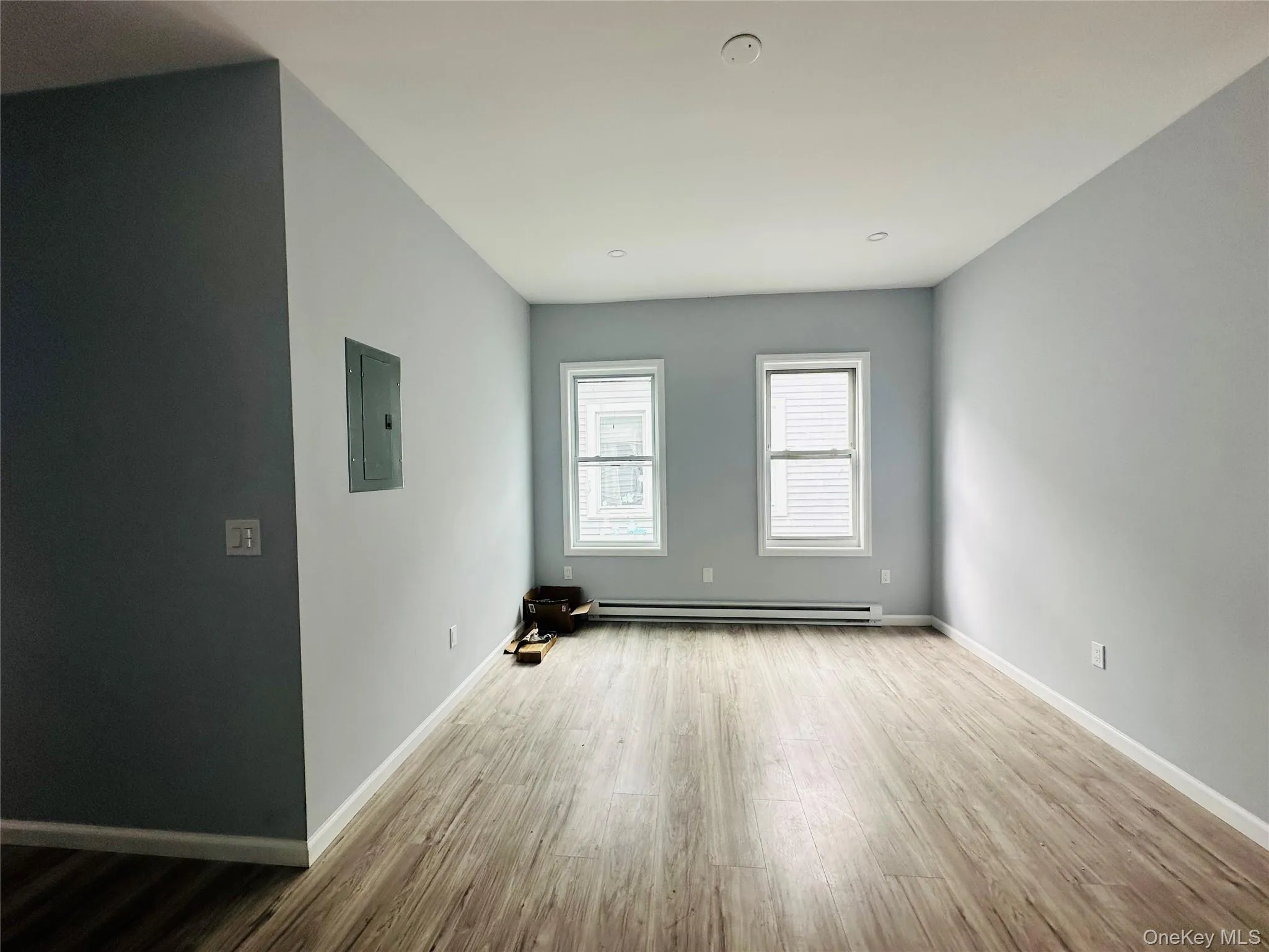 Unfurnished living room with wood finished floors, electric panel, and baseboard heating Unfurnished living room with wood finished floors, electric panel, and baseboard heating