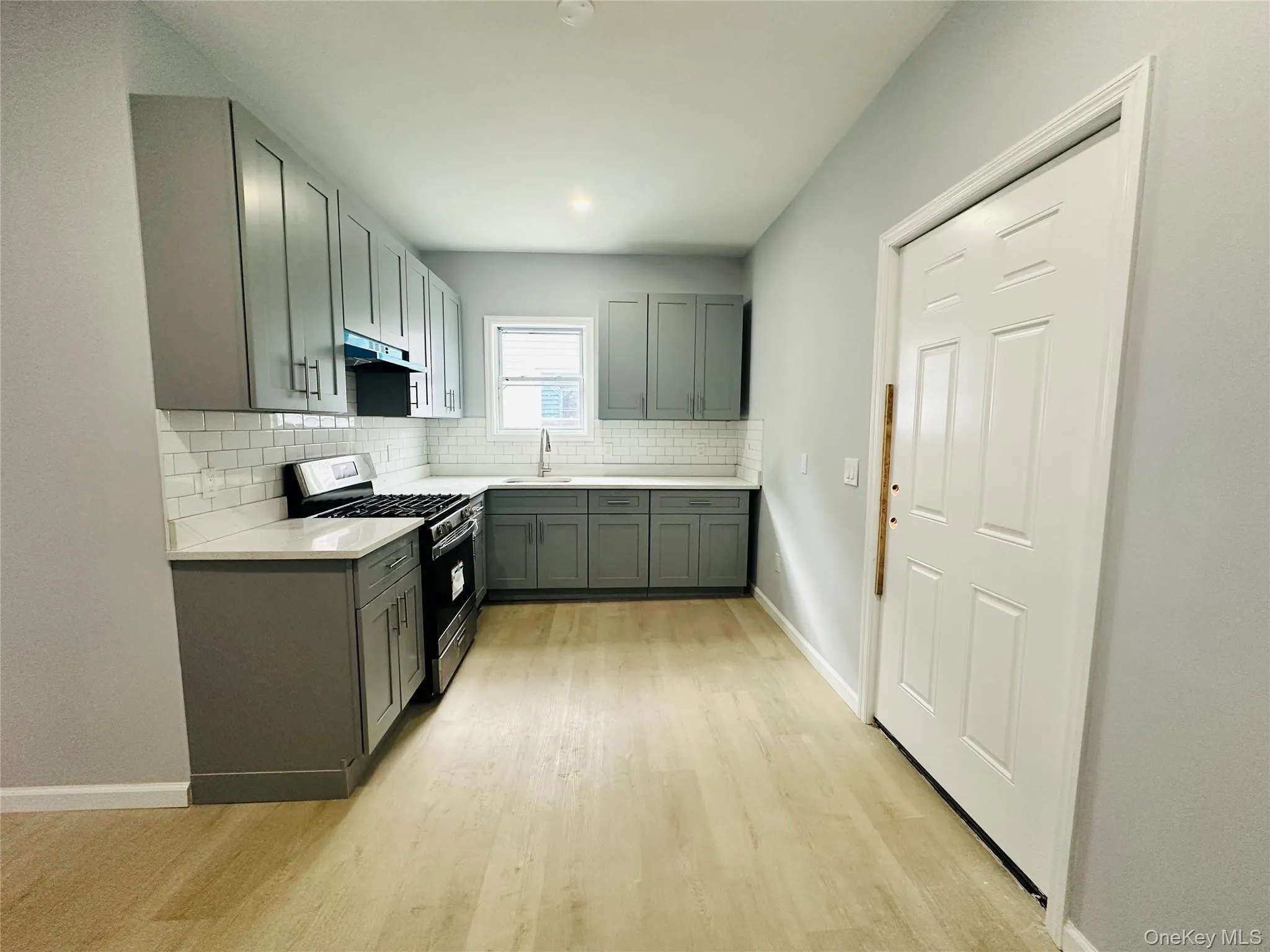 Kitchen with stainless steel range with gas cooktop, light wood-style flooring, backsplash, gray cabinetry, and under cabinet range hood Kitchen with stainless steel range with gas cooktop, light wood-style flooring, backsplash, gray cabinetry, and under cabinet range hood