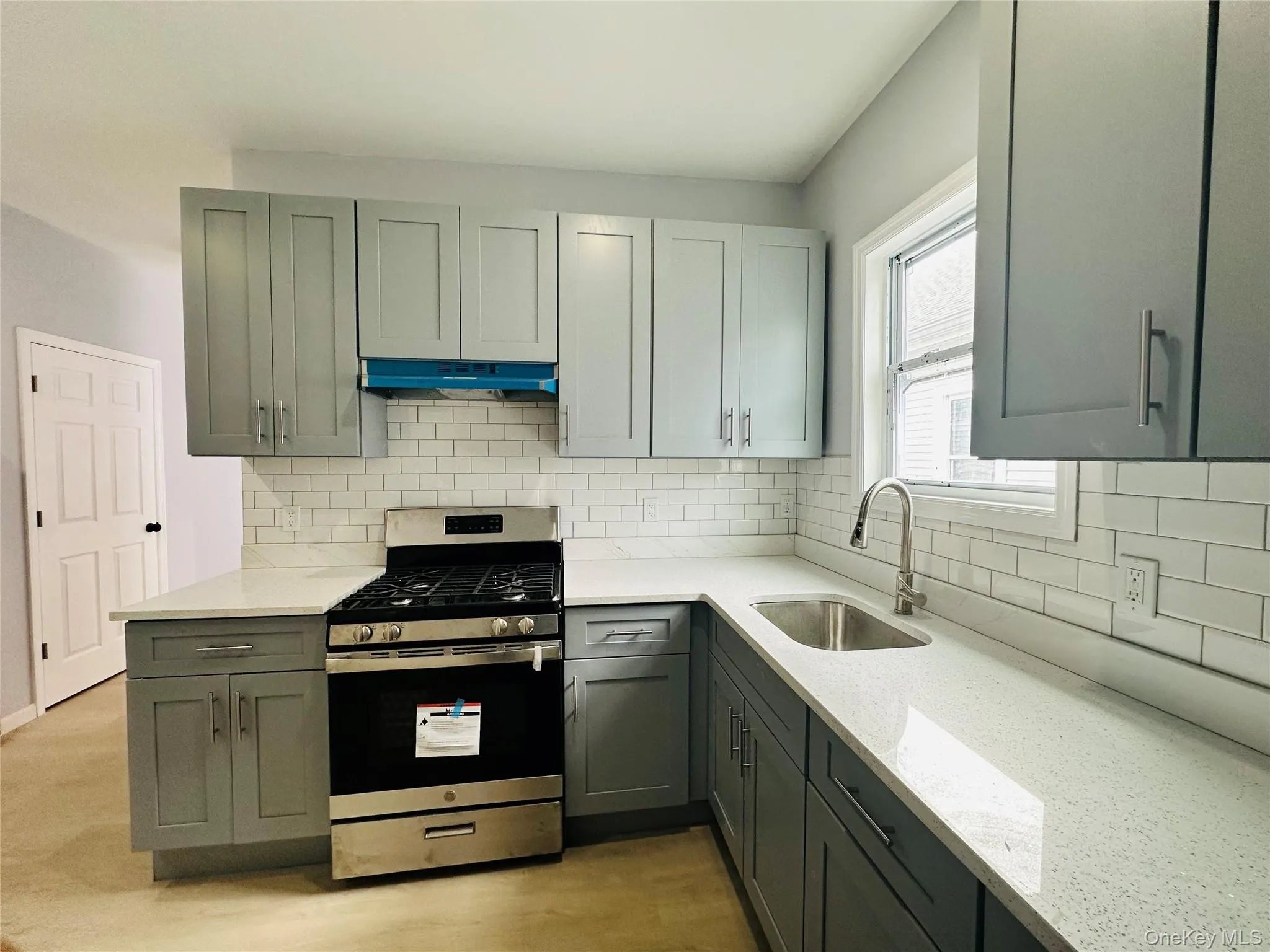 Kitchen with gas stove, light stone counters, tasteful backsplash, under cabinet range hood, and gray cabinetry Kitchen with gas stove, light stone counters, tasteful backsplash, under cabinet range hood, and gray cabinetry