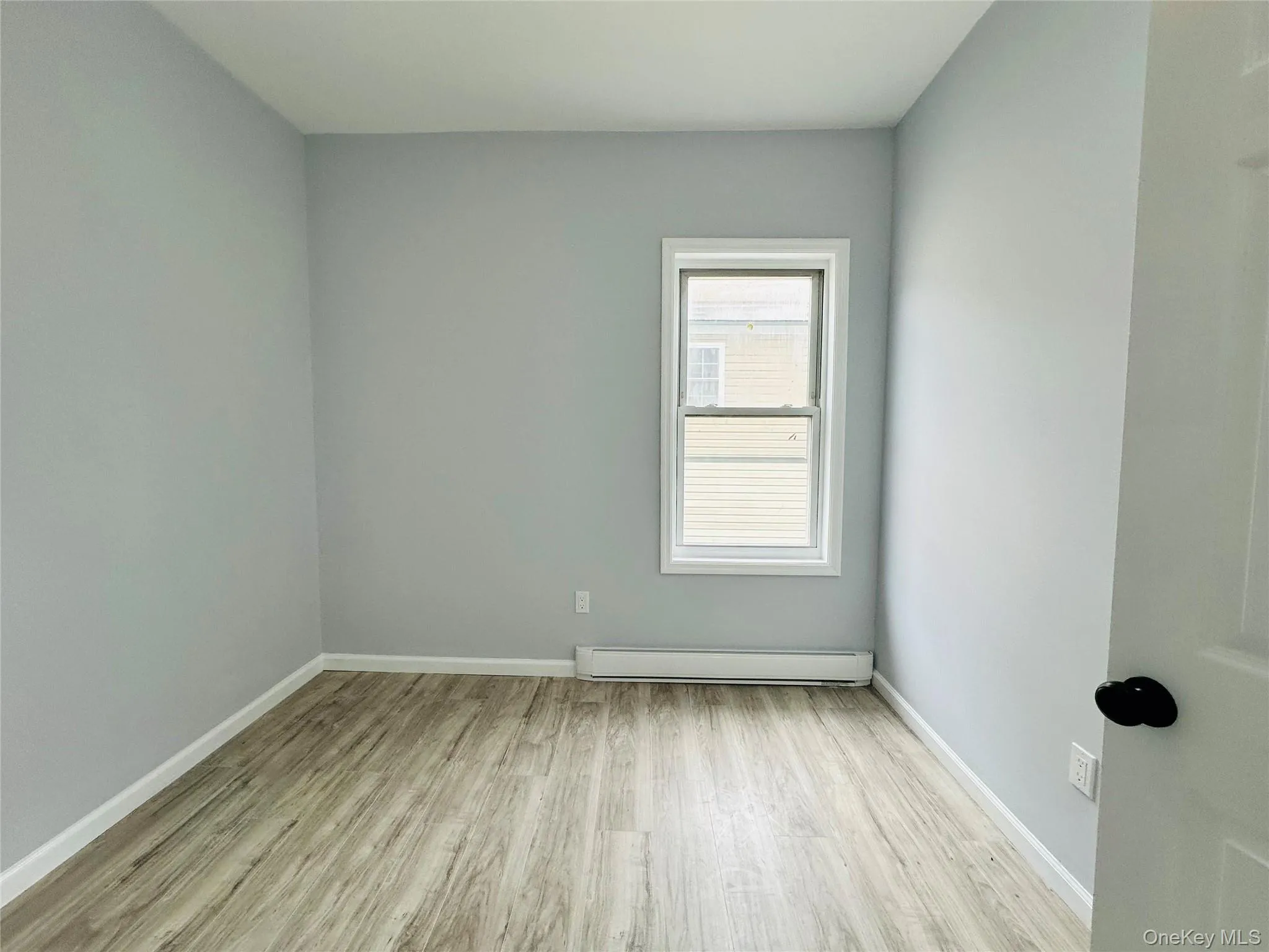 Empty room with light wood-style flooring and a baseboard radiator Empty room with light wood-style flooring and a baseboard radiator