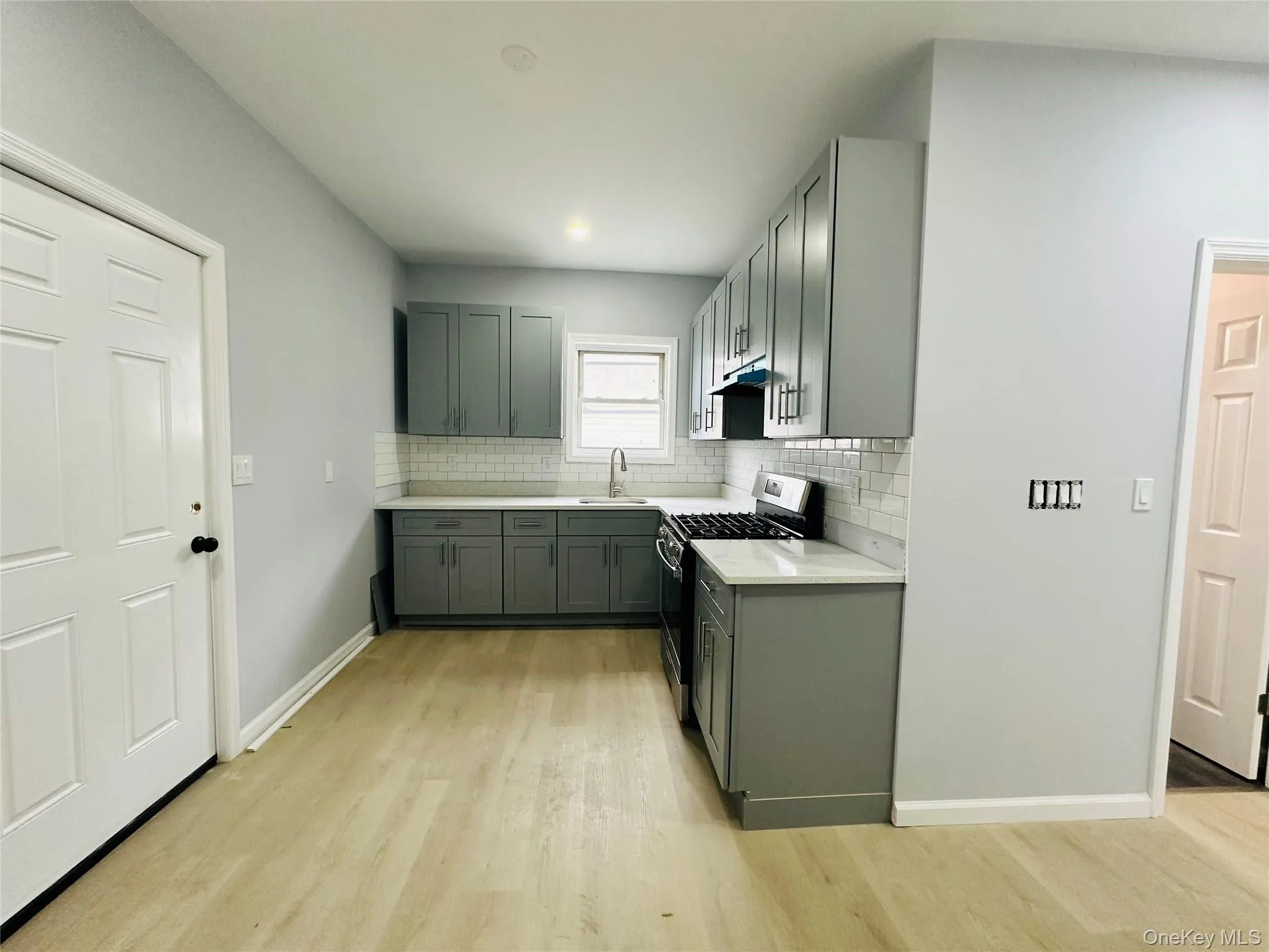 Kitchen featuring gas range, tasteful backsplash, light wood-style floors, light stone countertops, and gray cabinets Kitchen featuring gas range, tasteful backsplash, light wood-style floors, light stone countertops, and gray cabinets